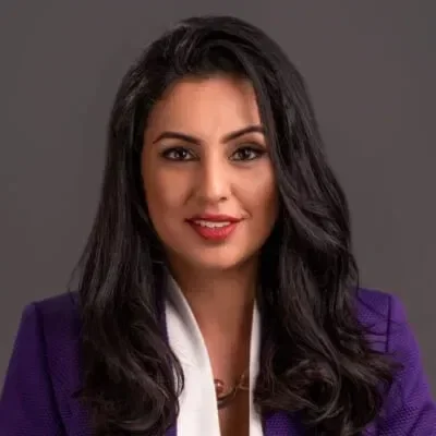 A woman with long black hair wearing a purple blazer and white blouse, smiling at the camera.