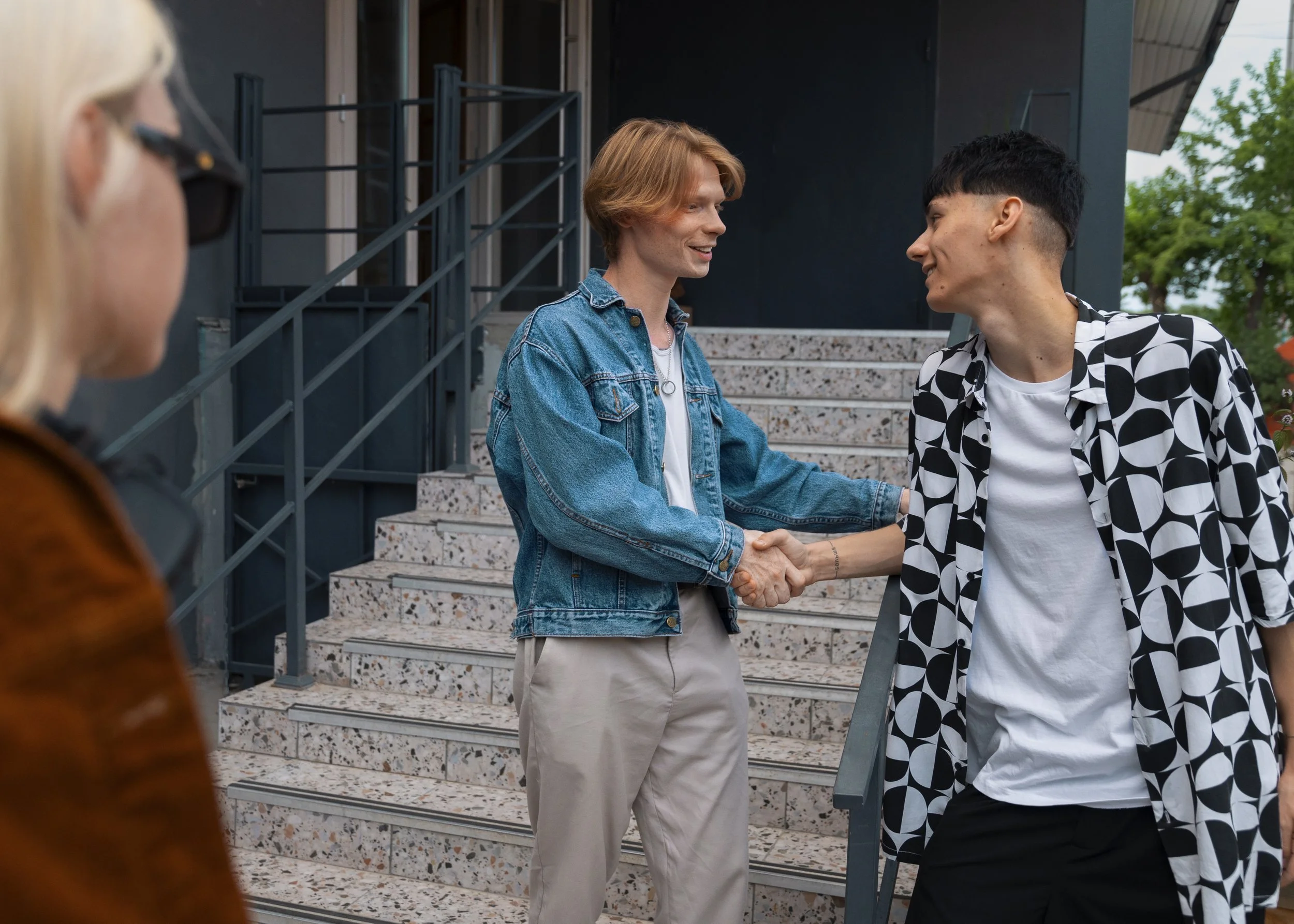 Five people silhouetted against a sunset sky, standing on rocks with arms raised and making peace signs.