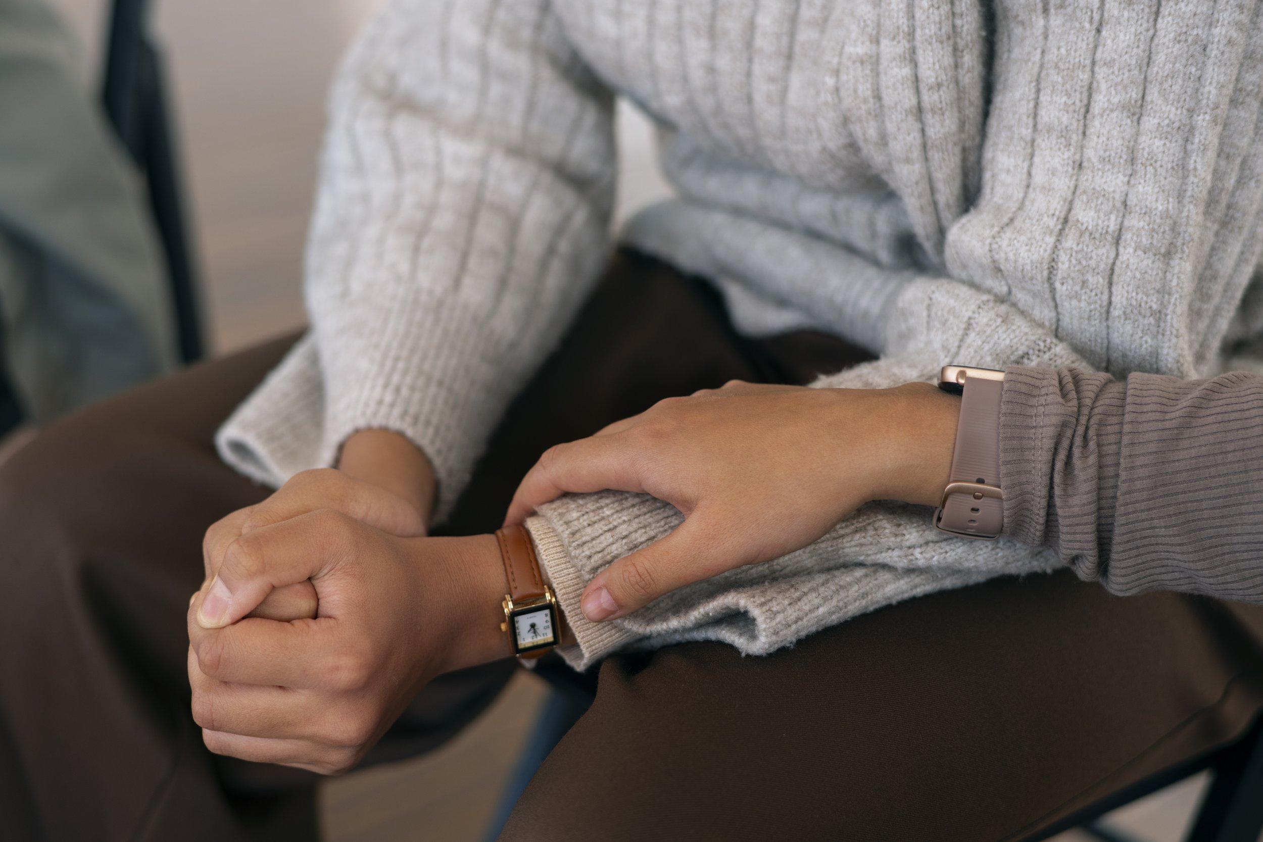 Close-up of two people holding hands, one wearing a dark sweater and smartwatch, the other wearing a white sweater, with an autumn forest background.