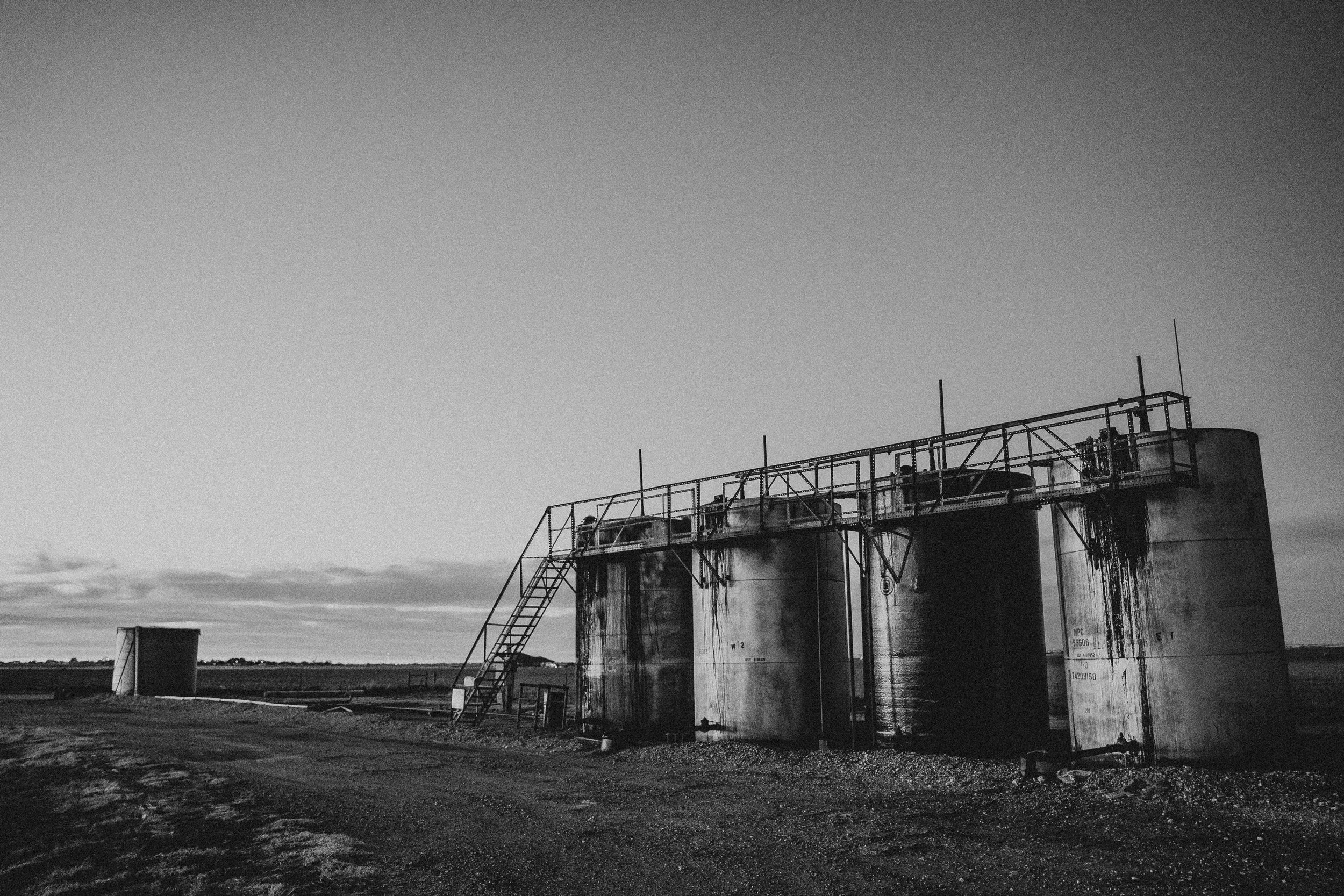Black and white photo of three large industrial storage tanks on a rural landscape at sunset.
