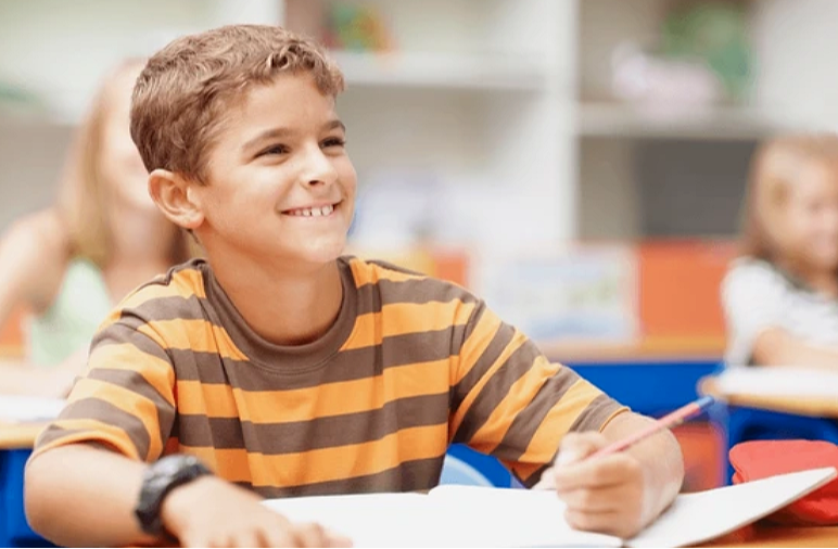 Smiling boy sitting calmly in a classroom, representing student confidence and emotional regulation.