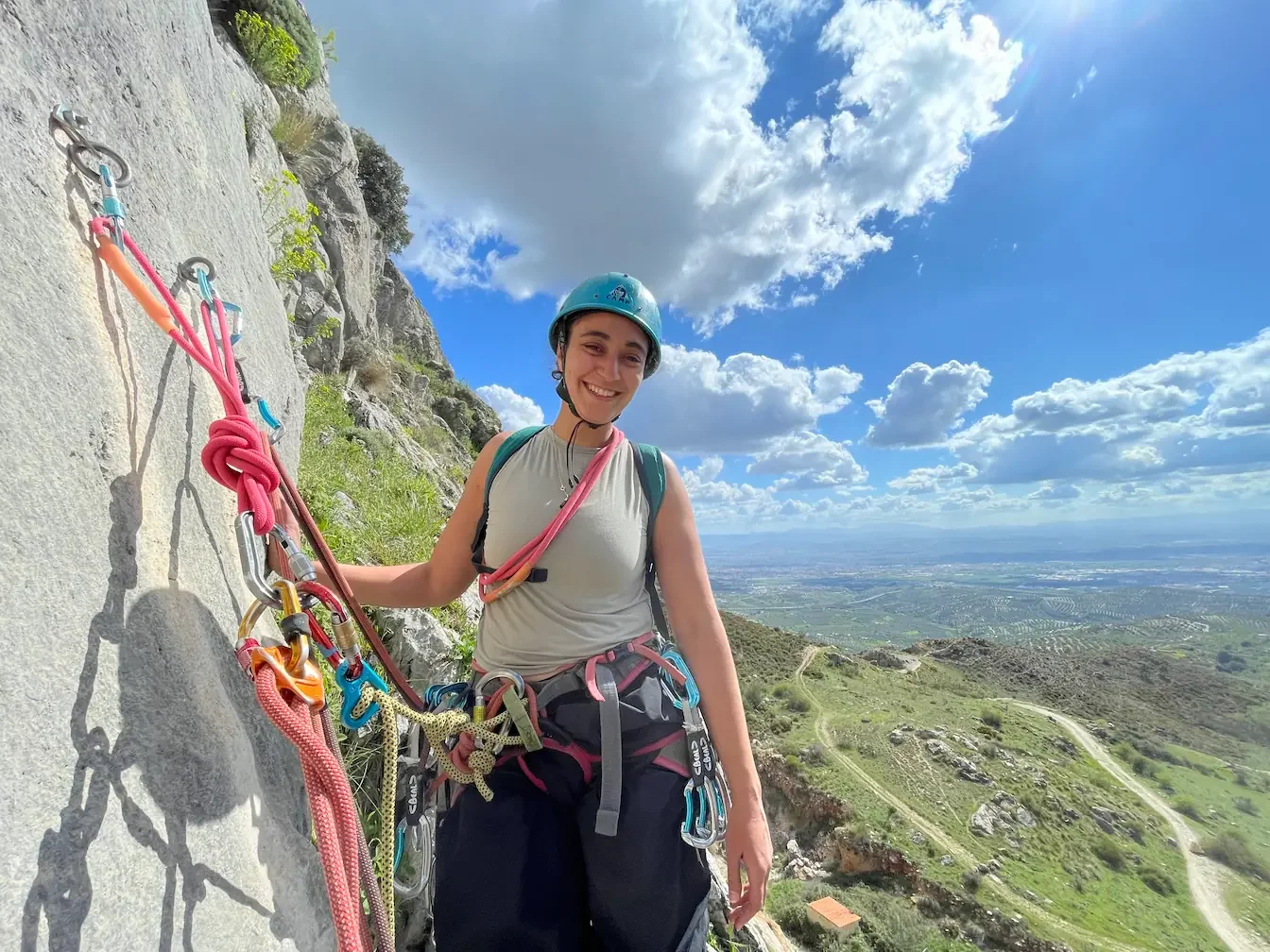 A girl smiling to the camera, proud of her first anchor she build during a multi-pitch course, Granada in the background