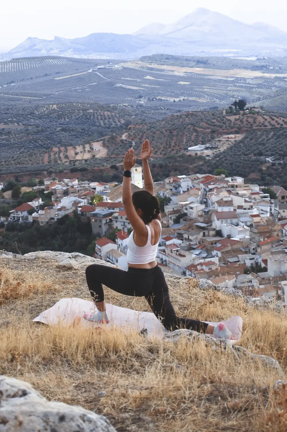 A woman practicing yoga on a hill overlooking a town  as part of climbing retreat in Granada