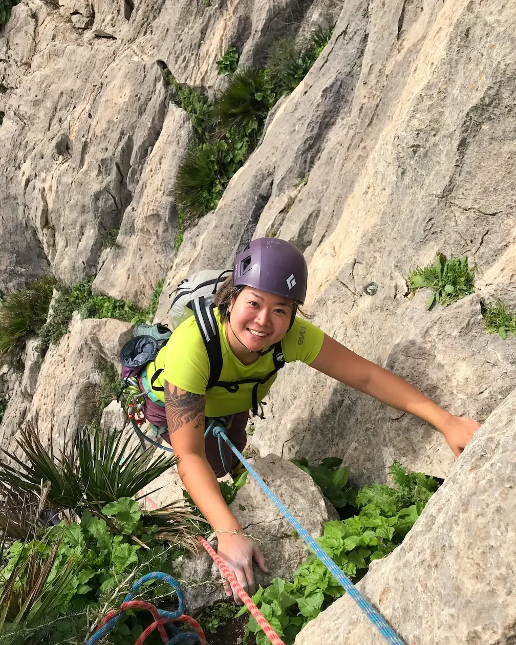 A girl happy to finish her first trad multipitch surrounded by tropical plants in el Chorro