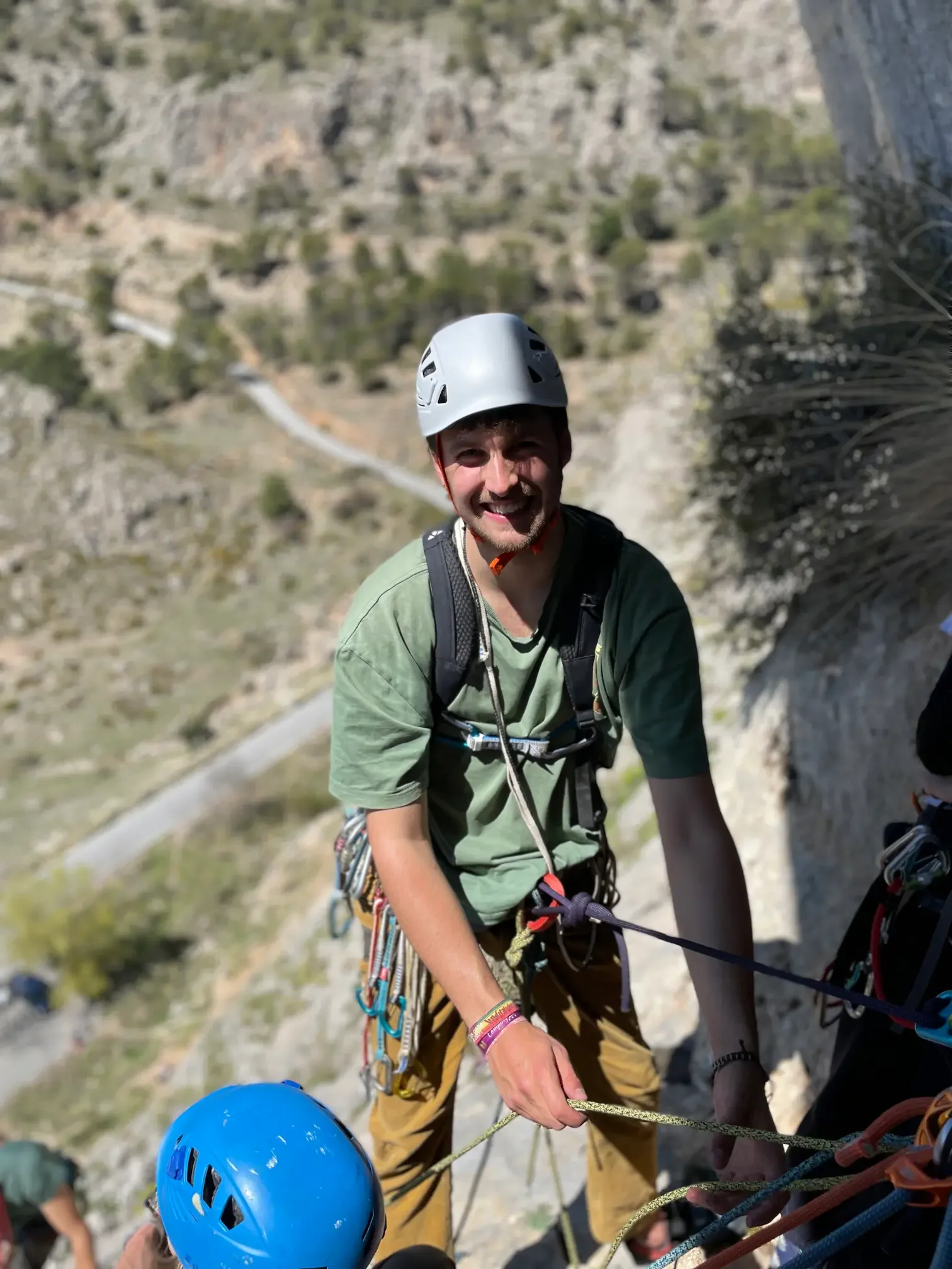 A guy at the final anchor of a multi-pitch, his getting ready to abseil, looking happy
