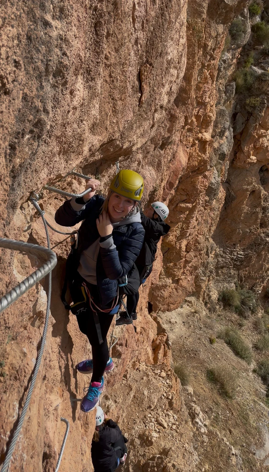 A girl smiling while progressing on the via ferrata of Guejar Sierra, orange rock in the background