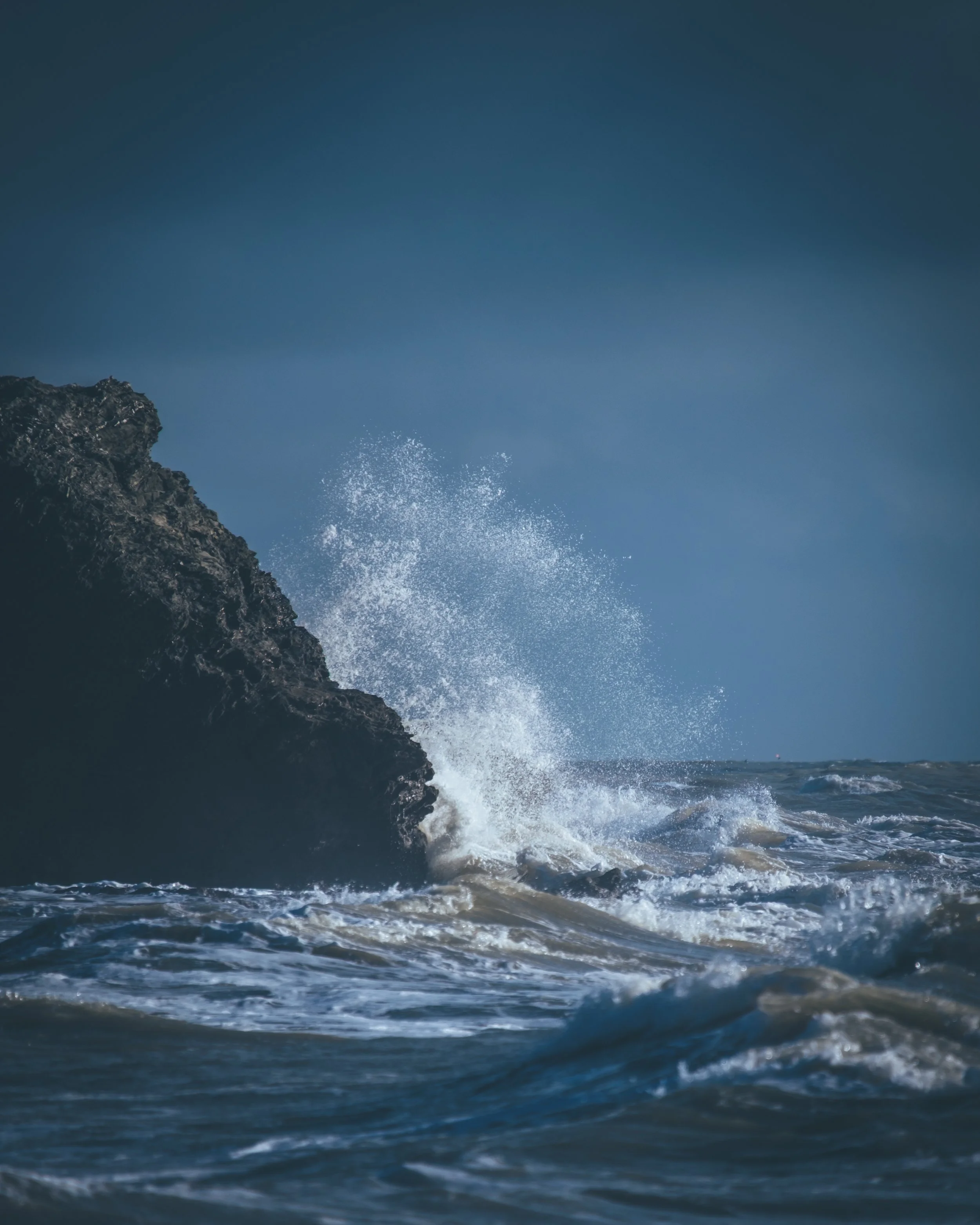 Vagues de mer frappant une roche en pleine mer under un ciel nuageux.