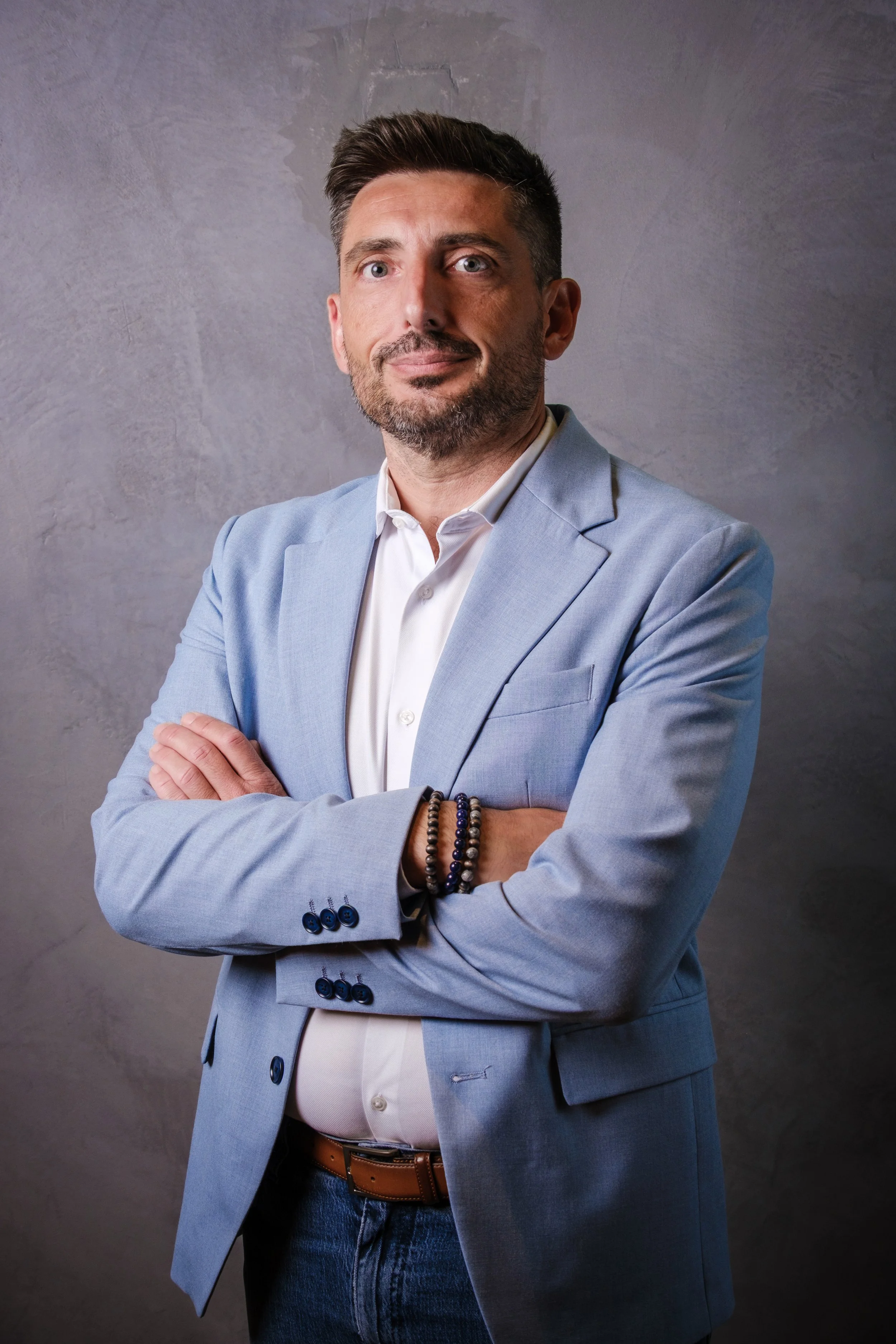 Homme d'affaires avec chemise blanche et veste bleue, bras croisés, bracelets, fond gris