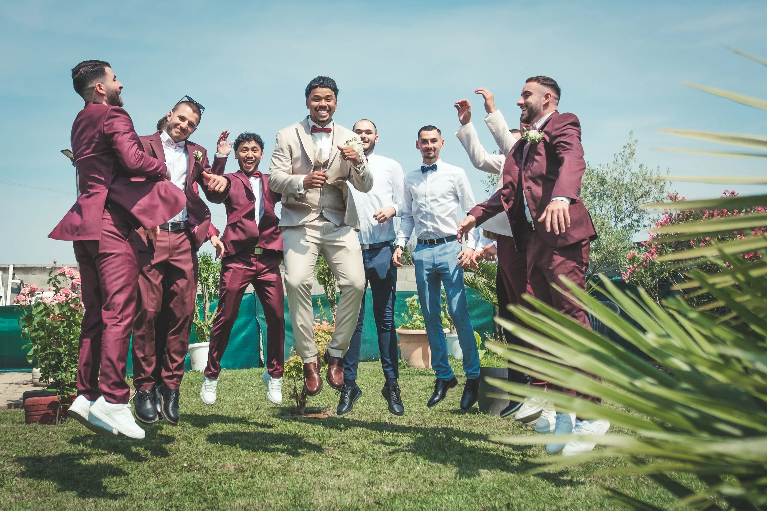 Groupe d'hommes en costumes sautant et souriant lors d'un mariage en plein air.