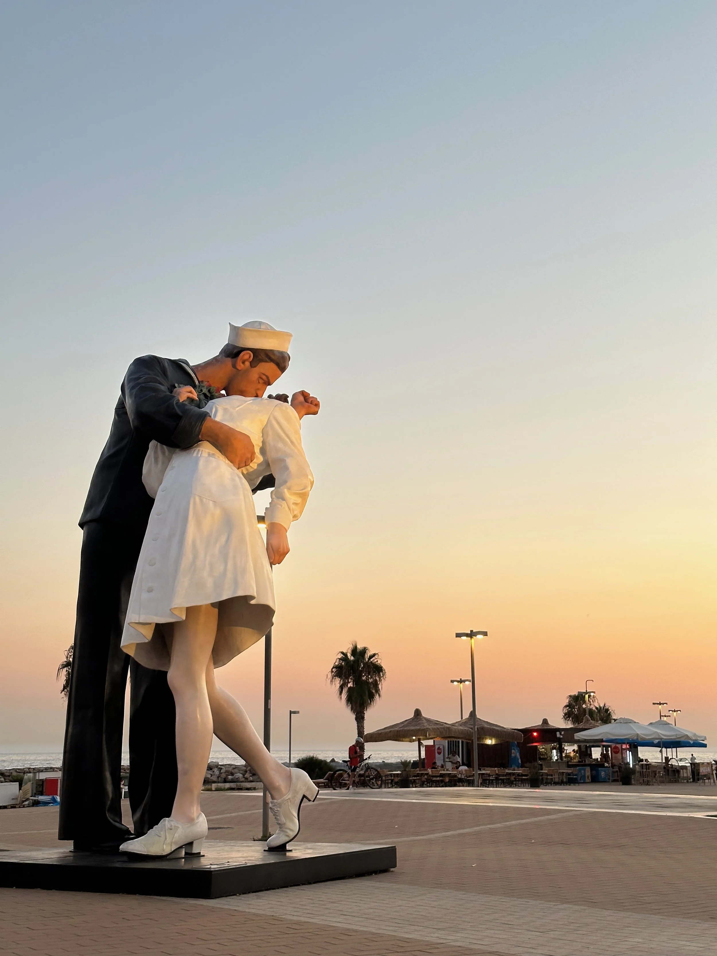 Statue de deux jeunes filles en uniforme de serveuses, l'une en tenue de marin, à côté de paysages de plage au coucher de soleil