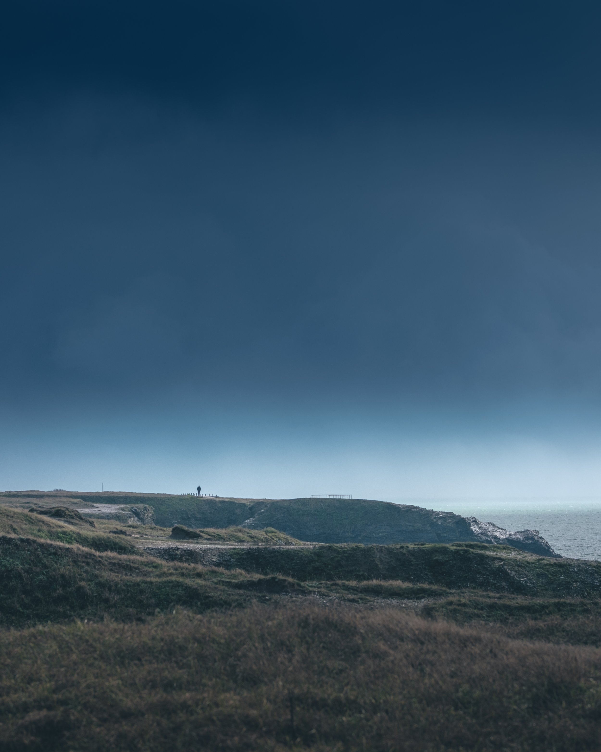 Un paysage côtier avec des falaises et un homme seul au sommet de la falaise, sous un ciel nuageux.