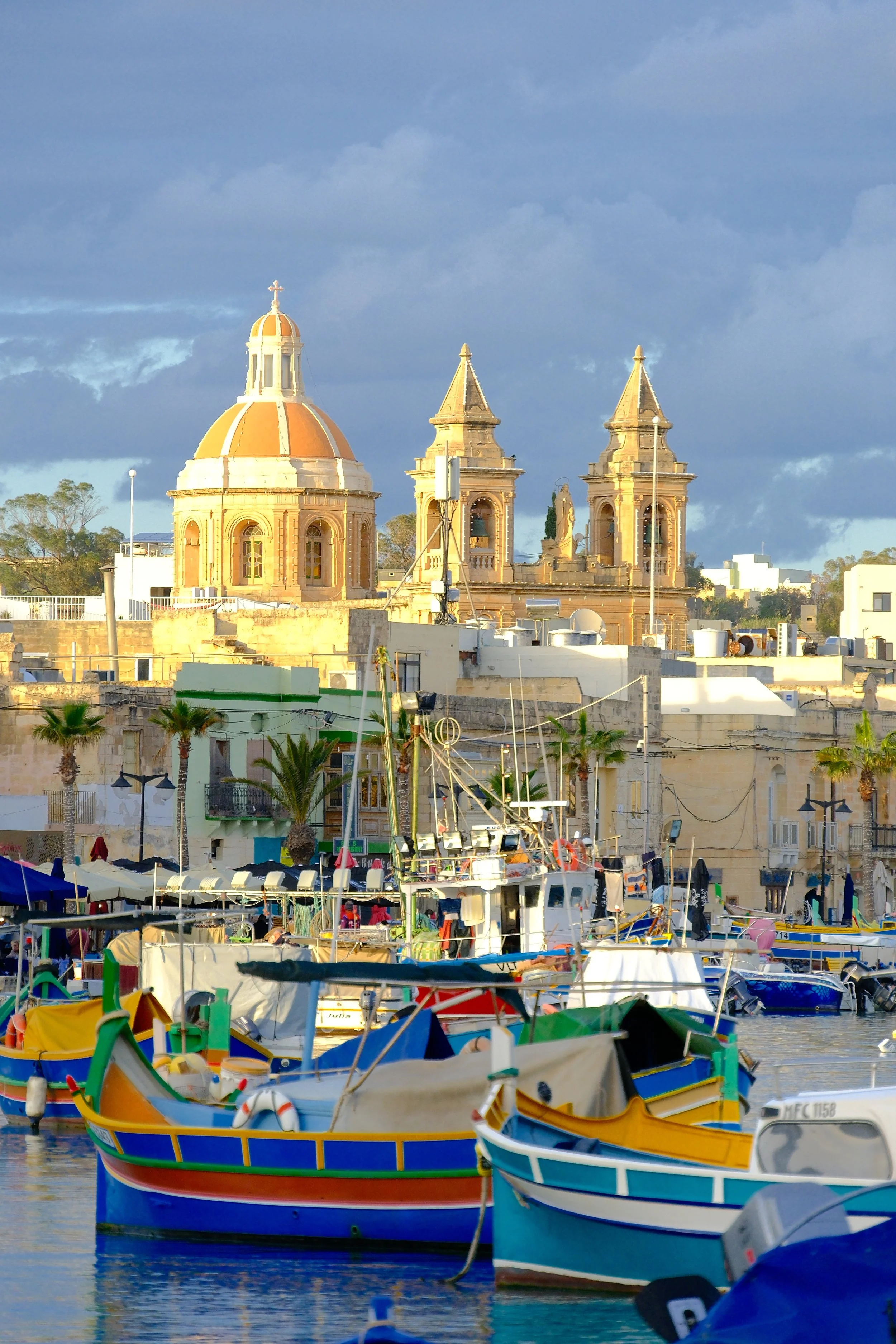 Un port avec des bateaux colorés devant une ville avec des églises ou des bâtiments historiques.