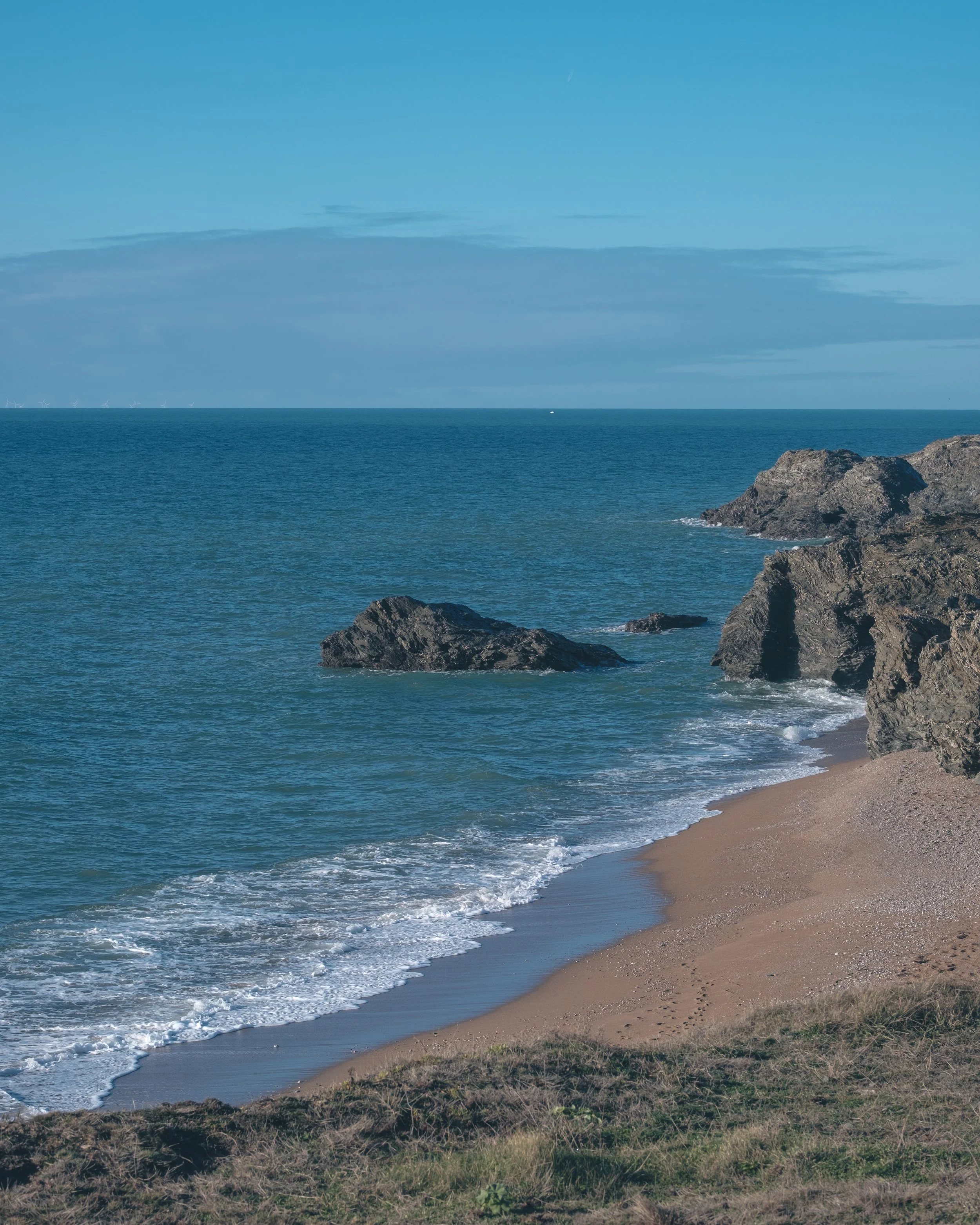 Plage de sable avec des rochers et la mer calme, ciel bleu avec quelques nuages