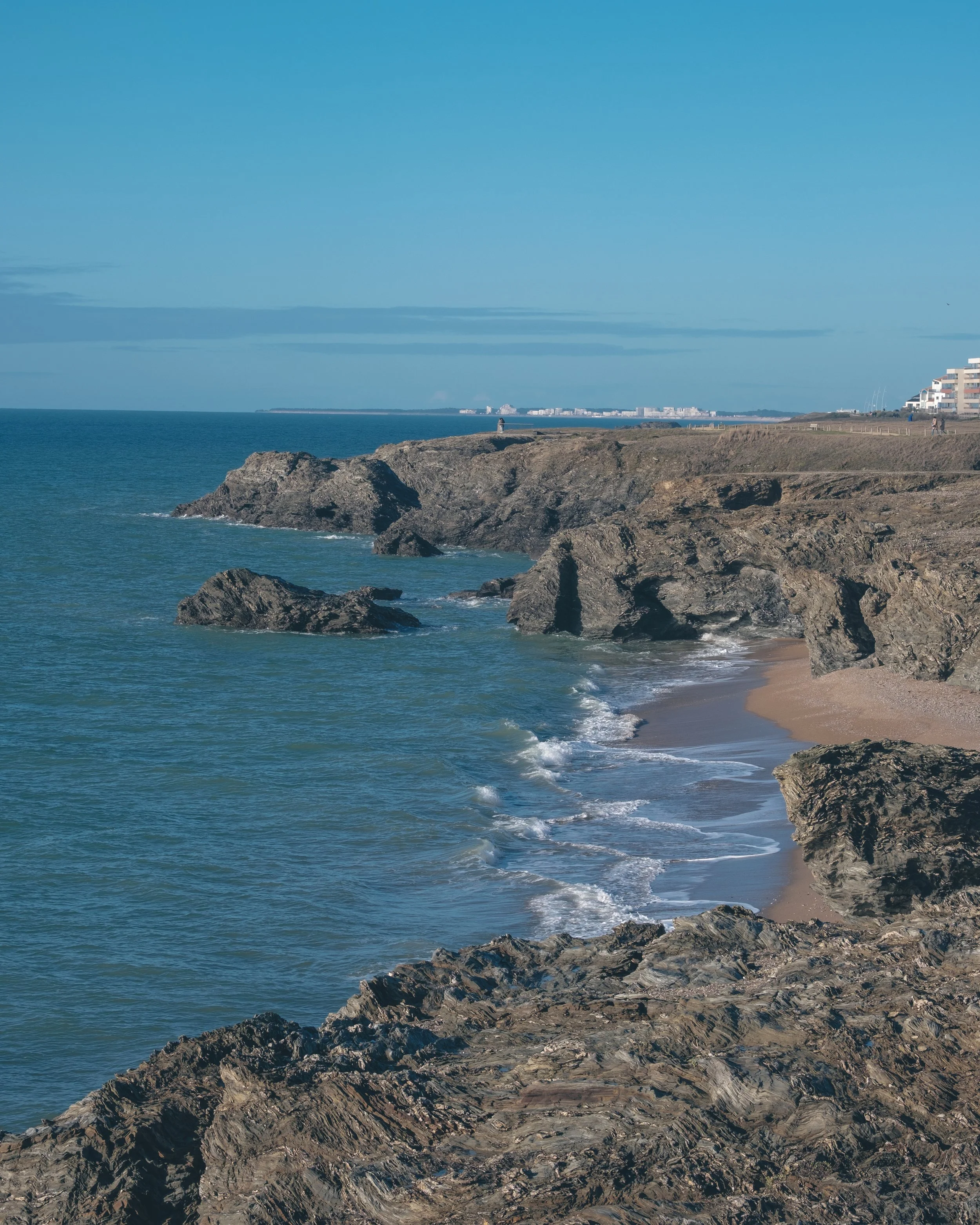 Côte rocheuse avec une plage de sable et la mer calme sous un ciel bleu.
