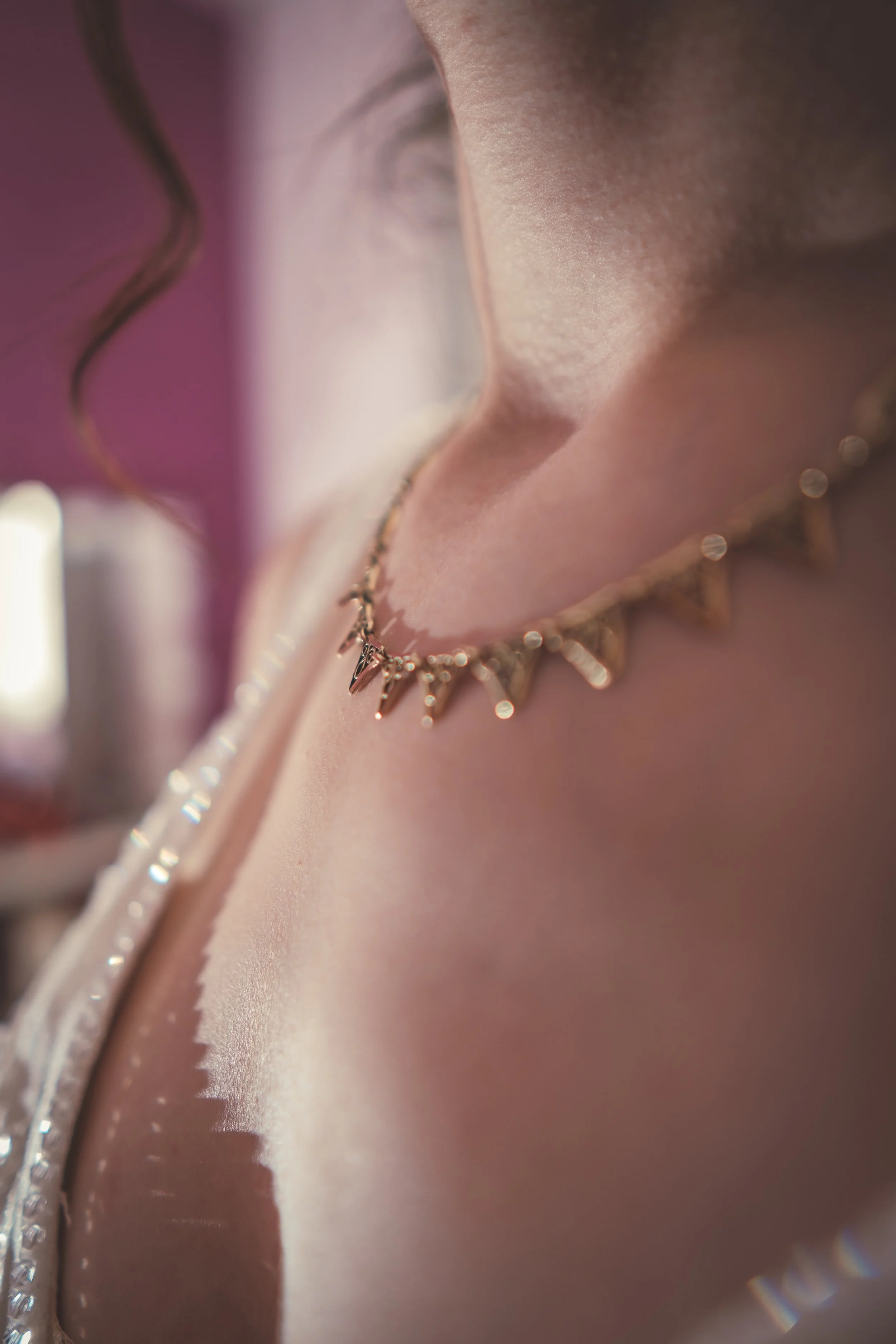 Détail d'une femme portant un collier à pointes doré et un maquillage subtil, avec une lumière douce.