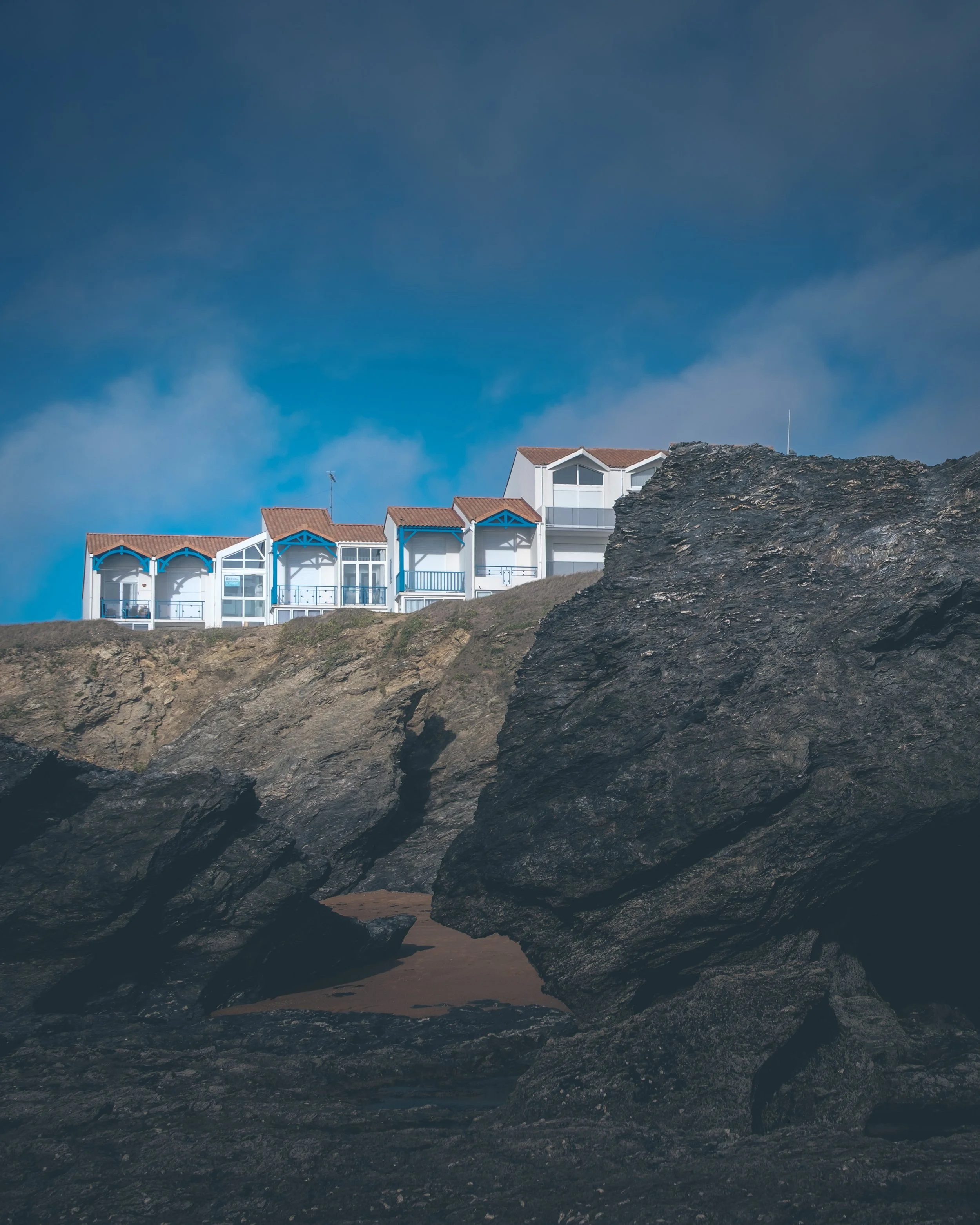 Maisons blanches avec toits en tuiles brunes sur une falaise rocheuse, sous un ciel bleu.