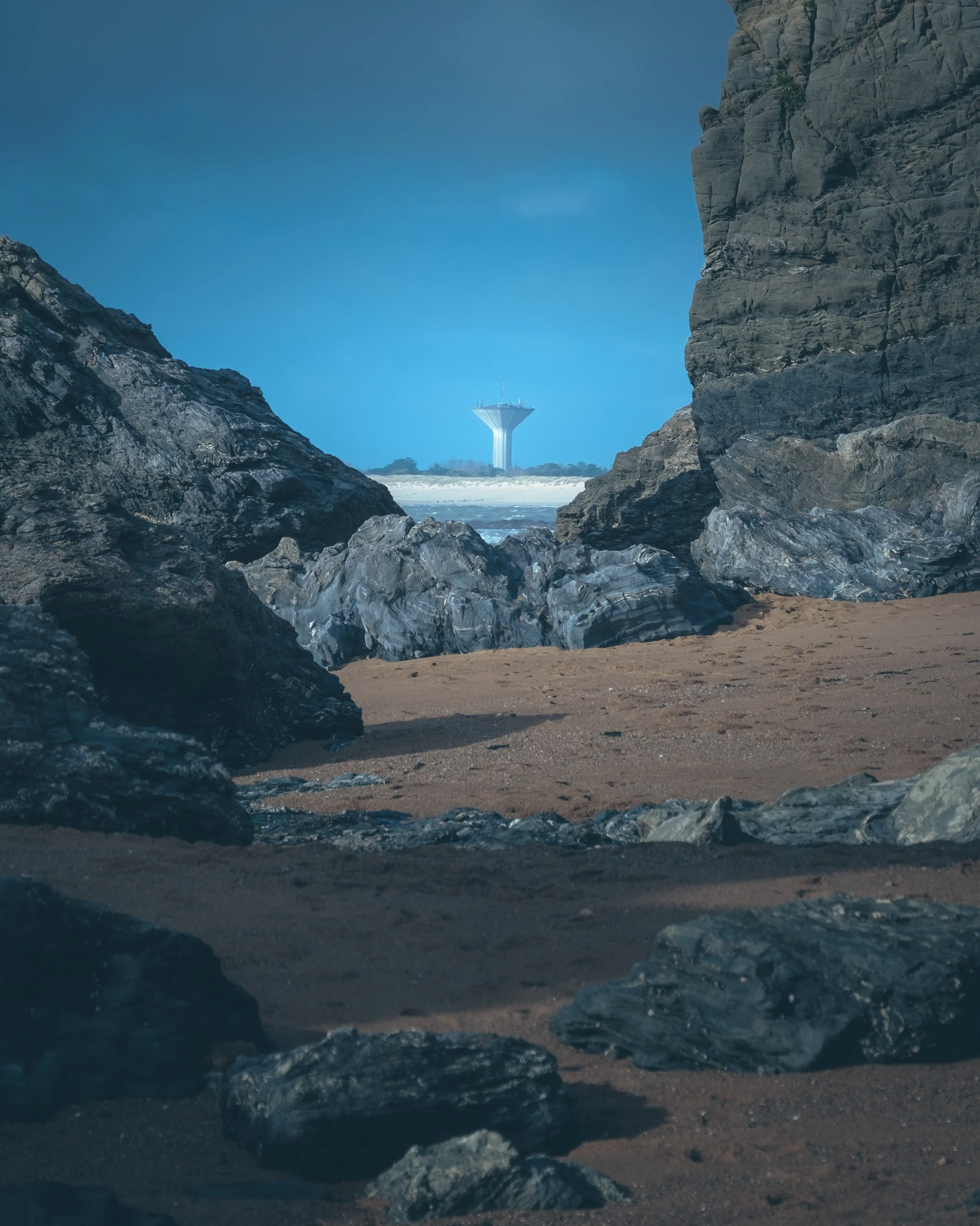 Vue d'une plage rocheuse avec une tour d'eau en arrière-plan, entre deux falaises rocheuses pendant une journée dégagée.