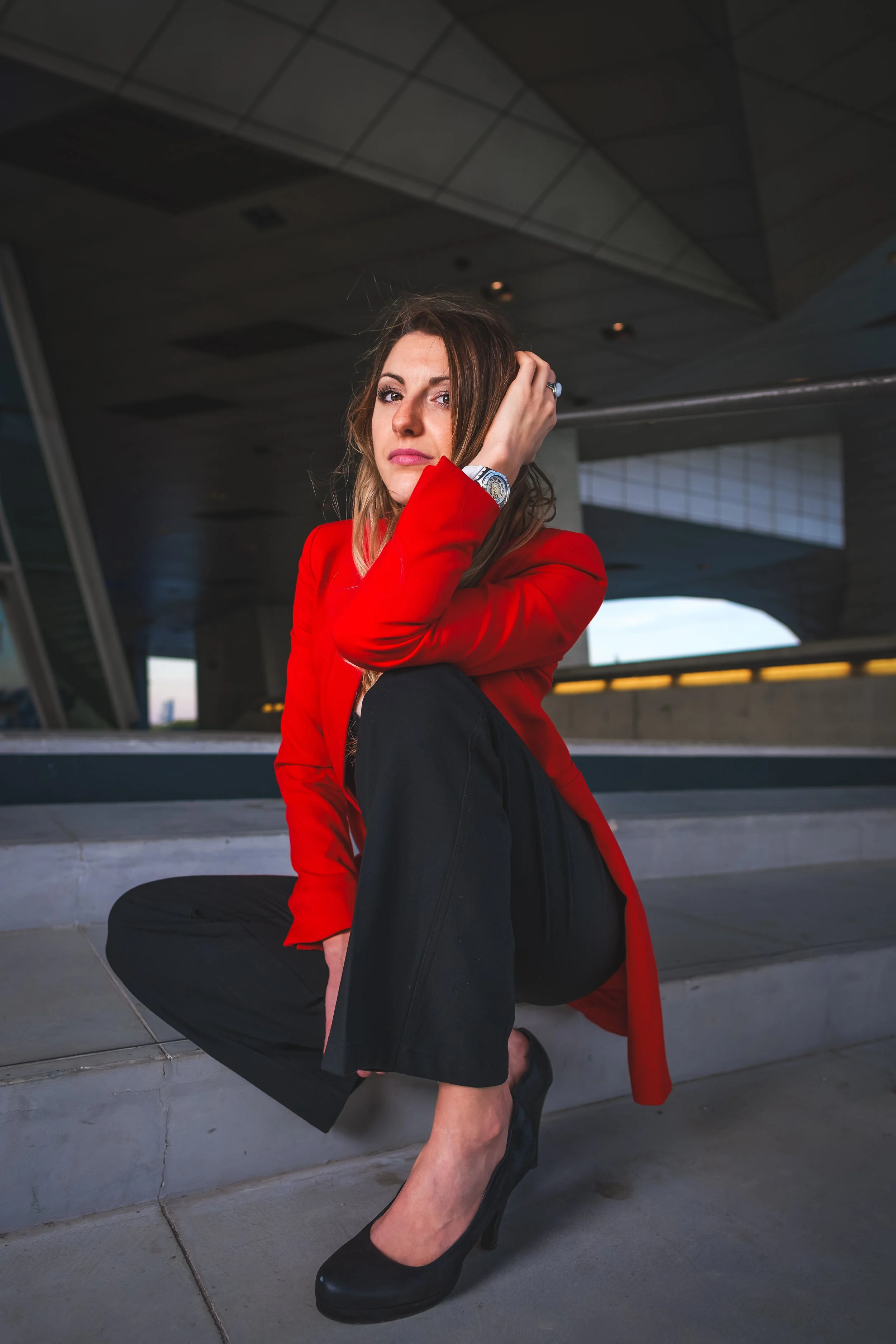 Femme en tailleur rouge assise sur des marches, sous un plafond en architecture moderne.