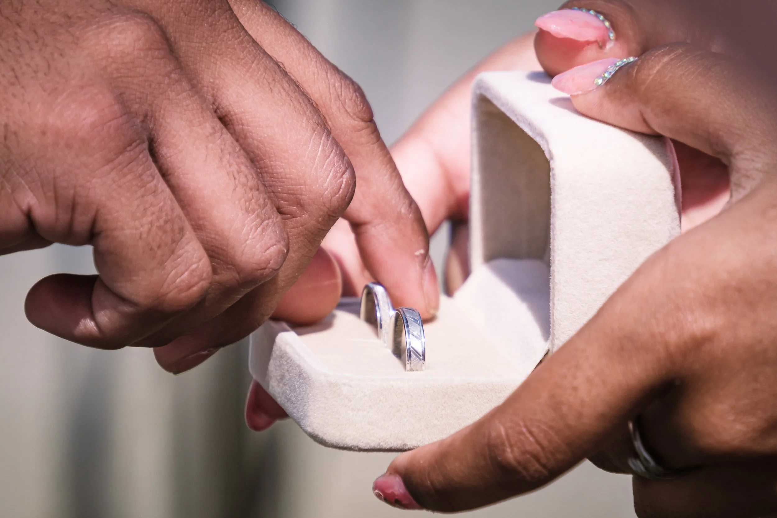 Deux mains, dont une avec un anneau, tenant une boîte à bijoux en velours beige avec des anneaux en argent à l'intérieur.