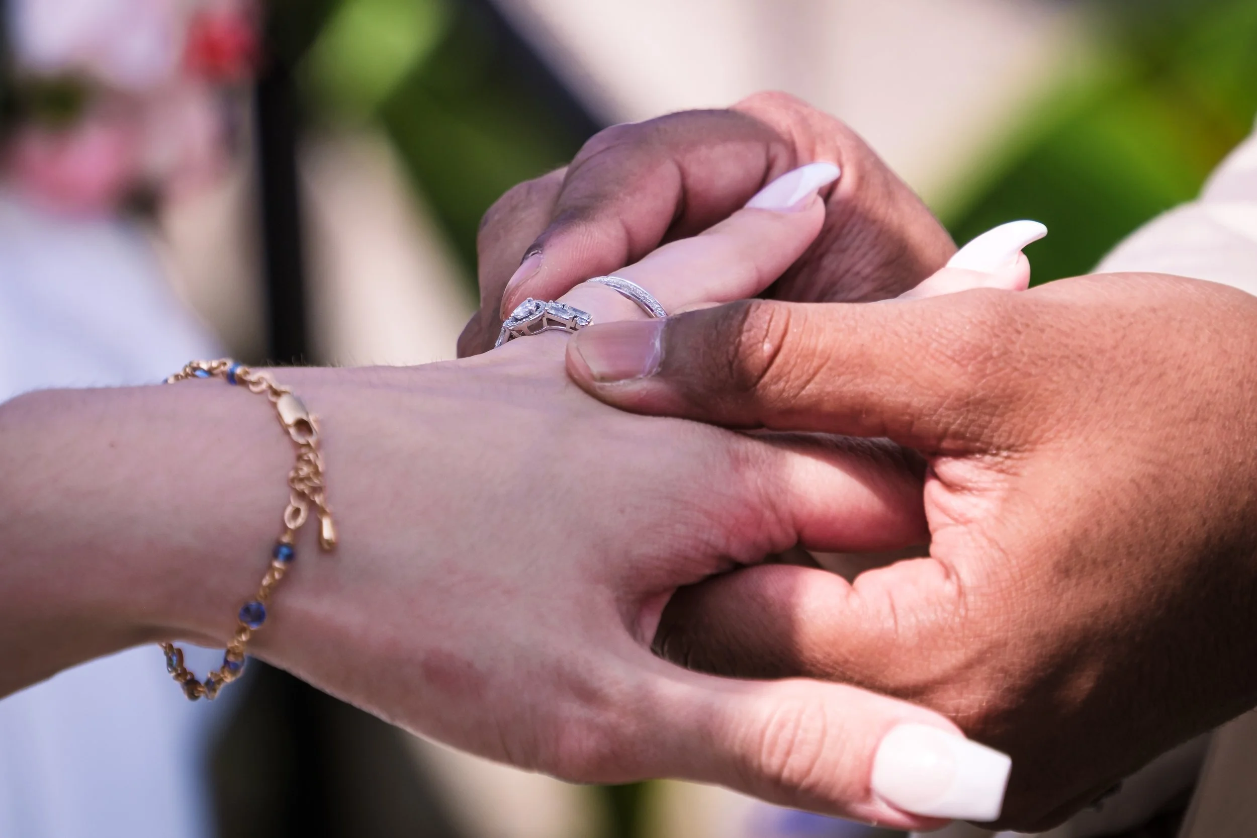 Une personne mariée tenant la main d'une autre personne dans un cadre extérieur, avec des bijoux visibles, suggérant un moment de mariage ou d'engagement.