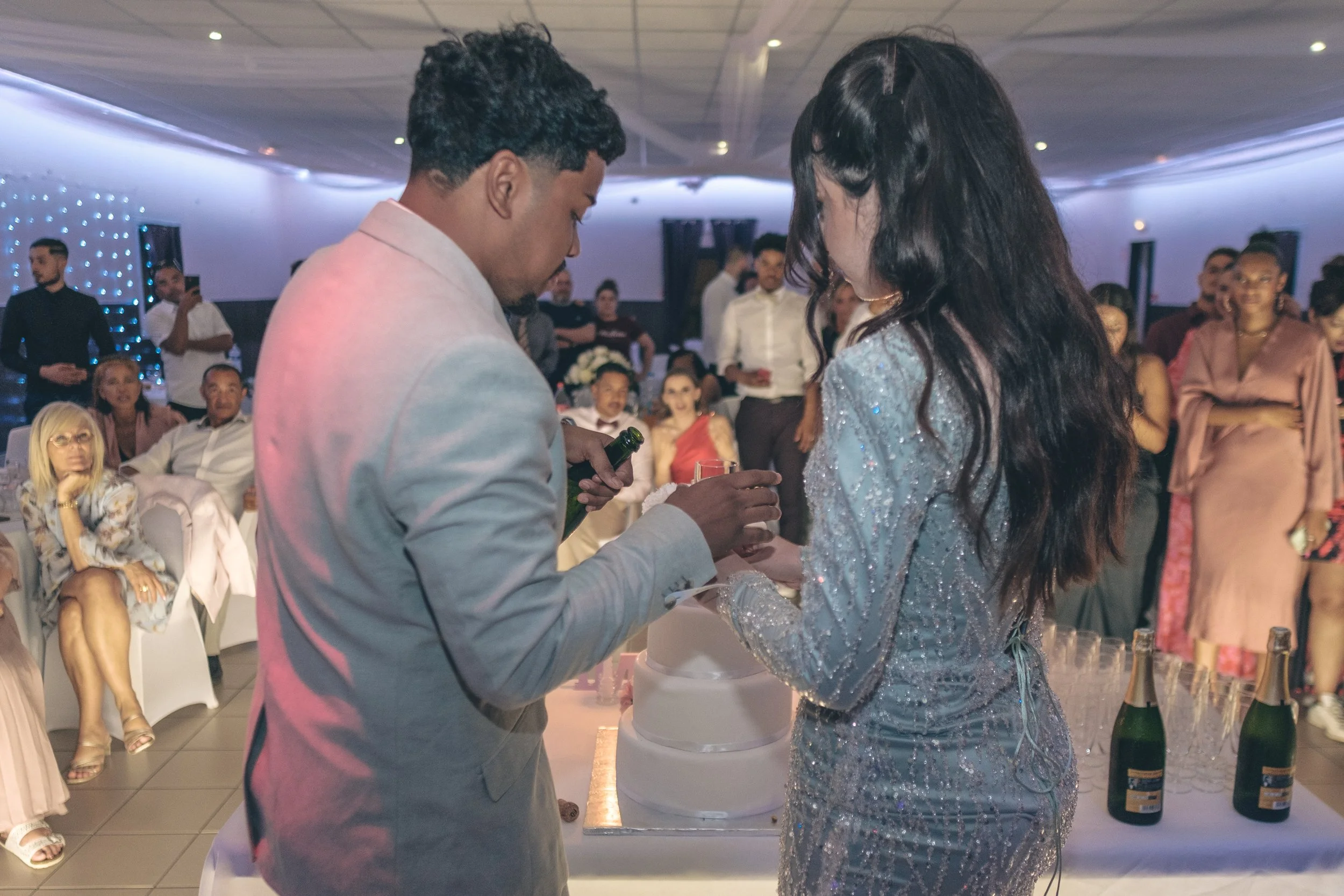 Un couple échange des alliances lors d'une cérémonie de mariage, entourés d'invités dans une salle décorée.