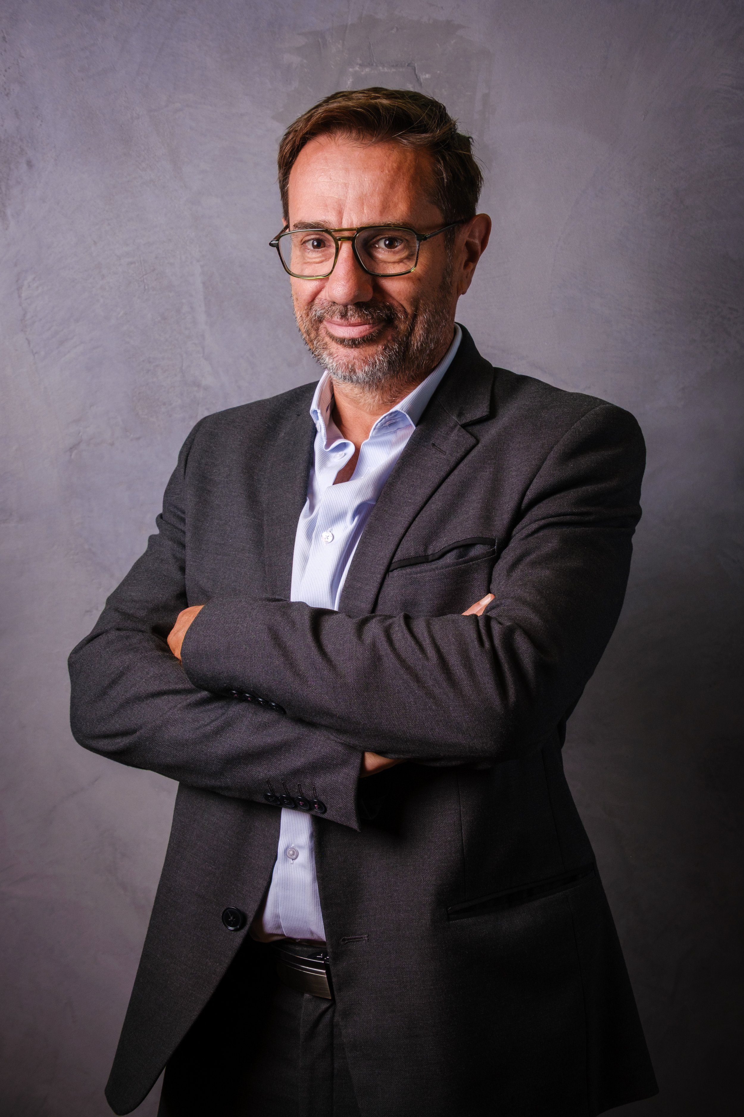 Homme d'affaires portant un costume gris, chemise blanche, lunettes, avec des bras croisés, fond gris