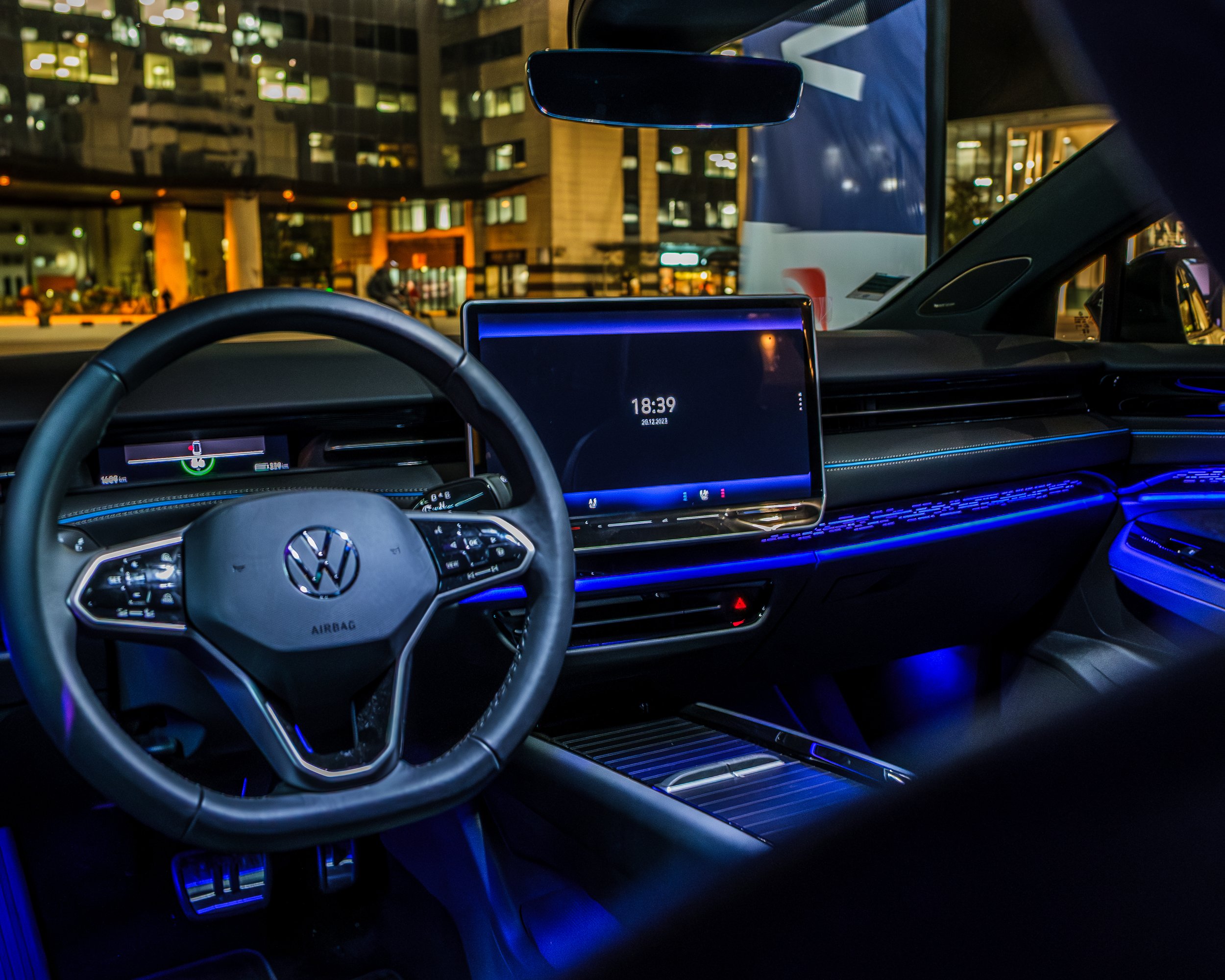Intérieur d'une voiture Volkswagen avec un tableau de bord numérique et un grand écran tactile, illuminated par des lumières bleues dans un environnement urbain la nuit.