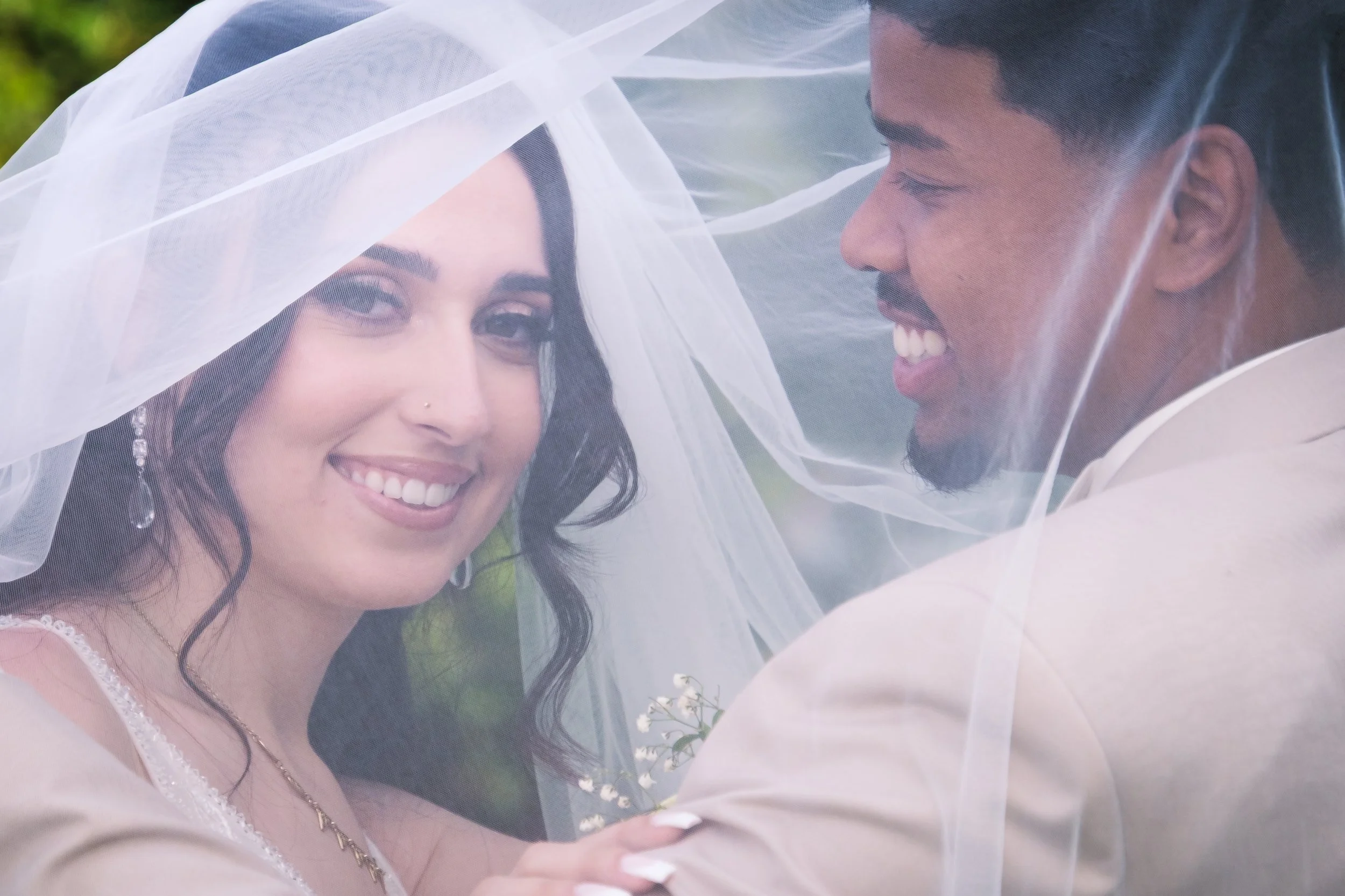 Un couple de mariés sous un voile de mariée qui sourient.