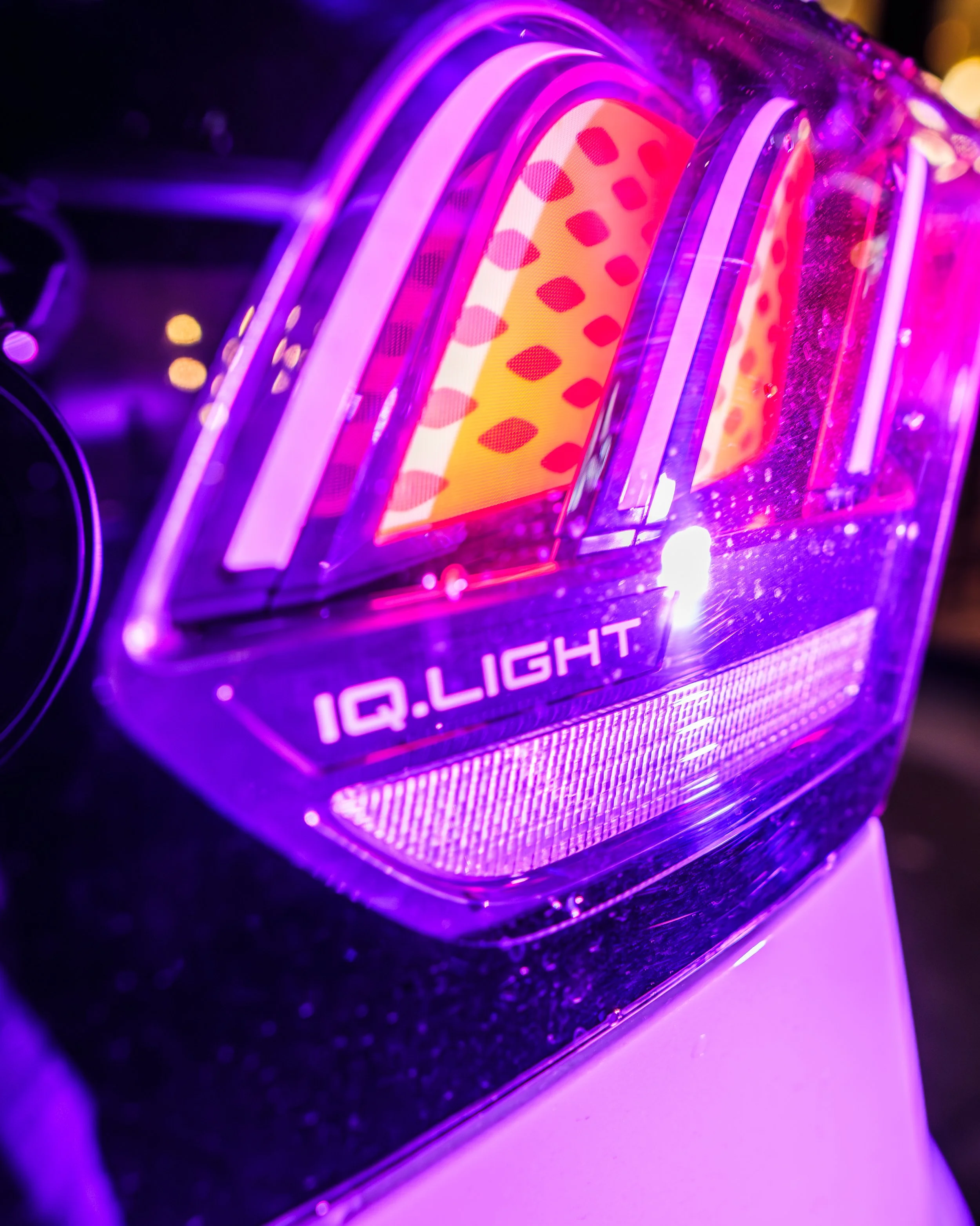 Gros plan d'un écran LED coloré vibrant avec la mention "IQ Light" sous une lumière violette et des motifs en forme de gouttes oranges et rouges.