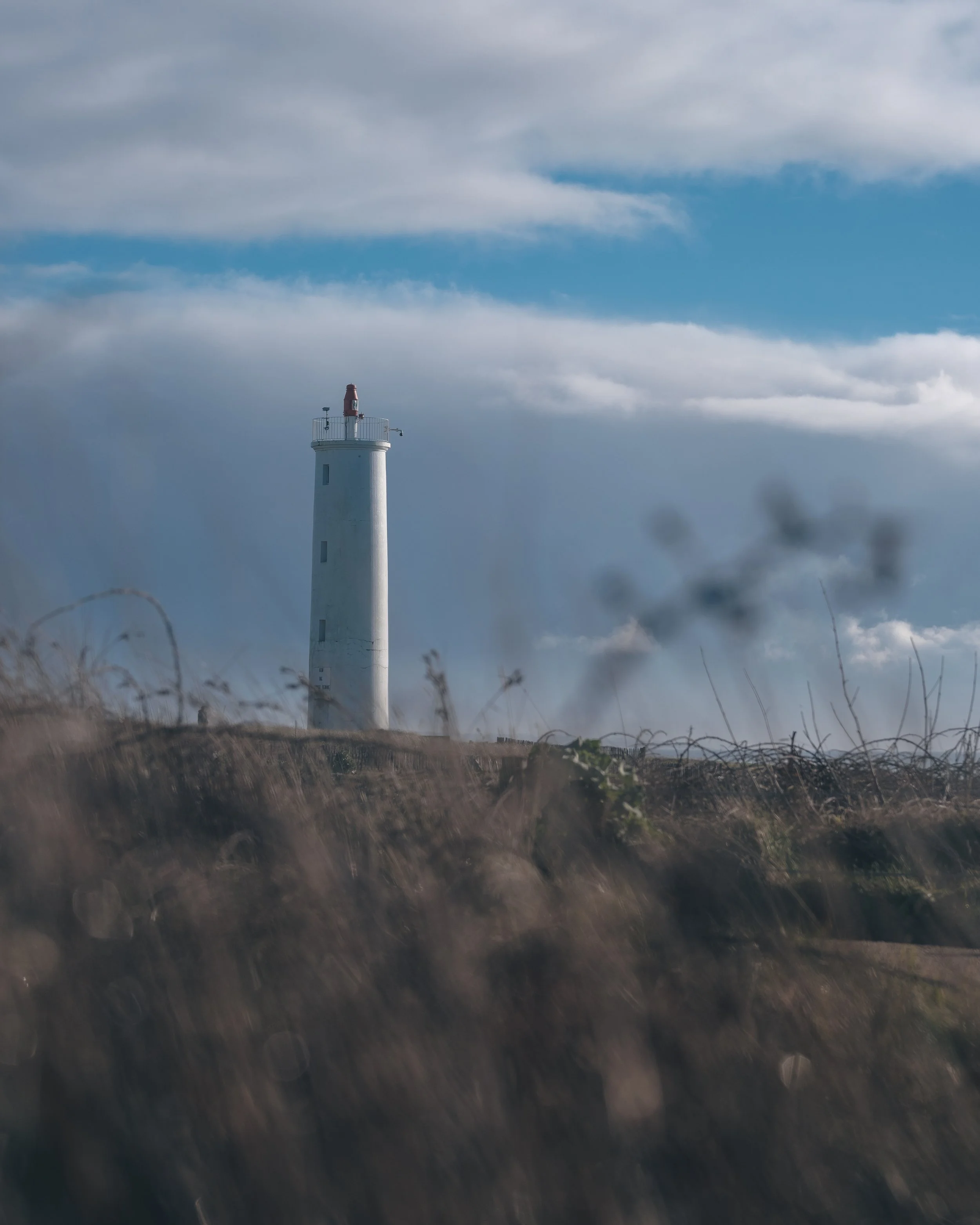 Phare blanc sur une côte rocheuse sous un ciel partiellement nuageux