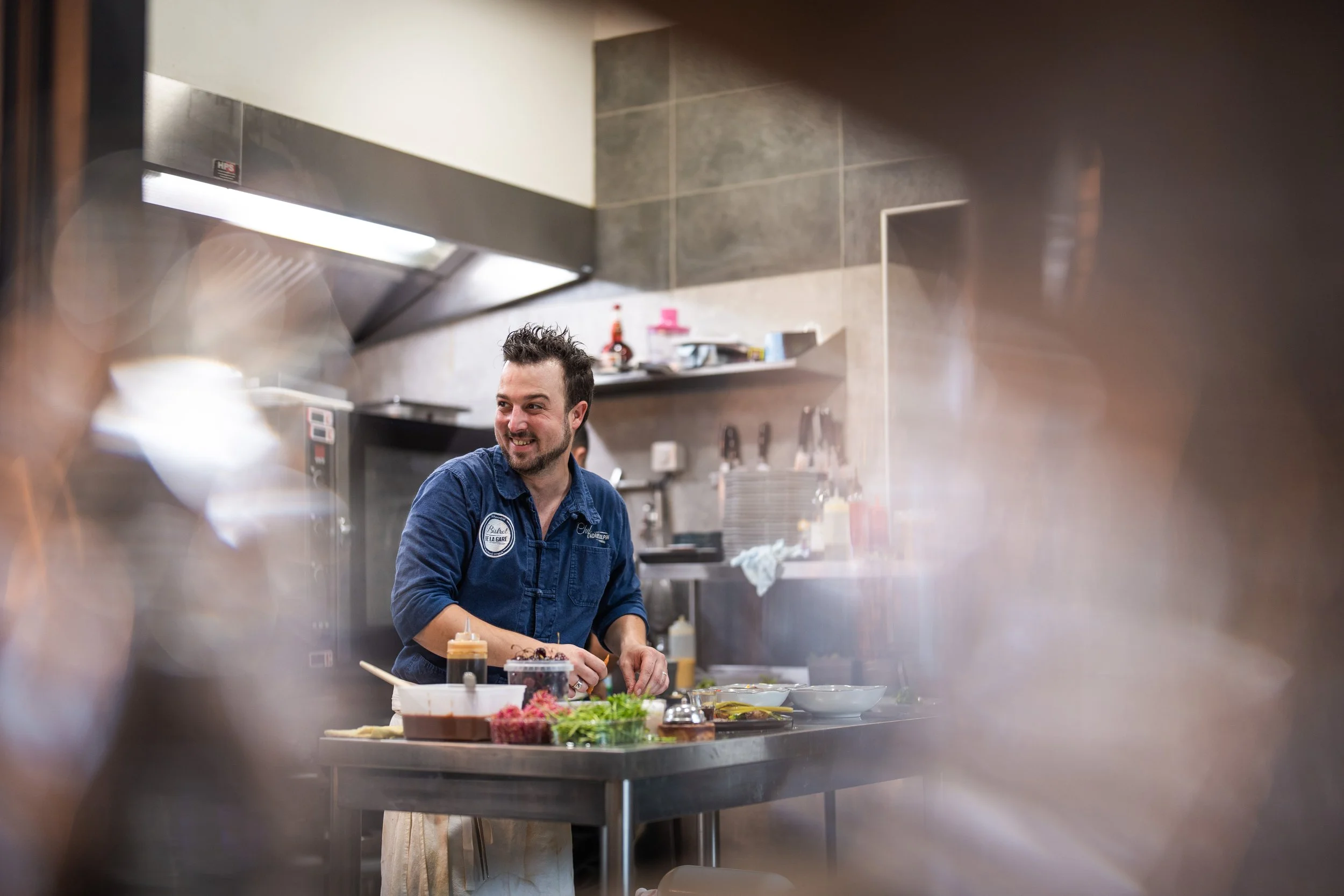 Un chef souriant dans une cuisine professionnelle, entouré d'ingrédients et d'ustensiles de cuisine.