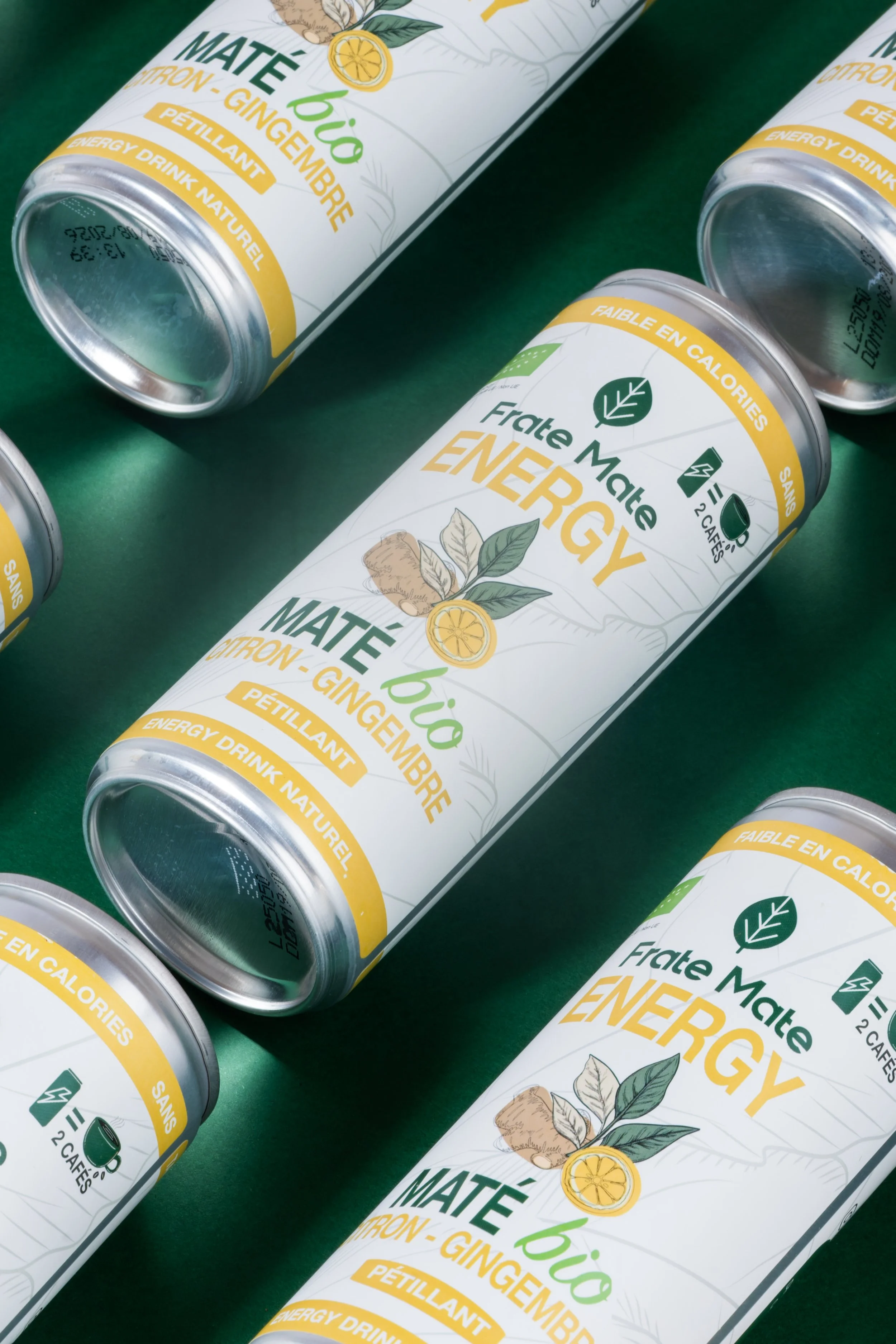 Cannes de boisson énergisante bio au citron, gingembre et pétillant, de la marque Frate Mate, posées sur une surface verte.