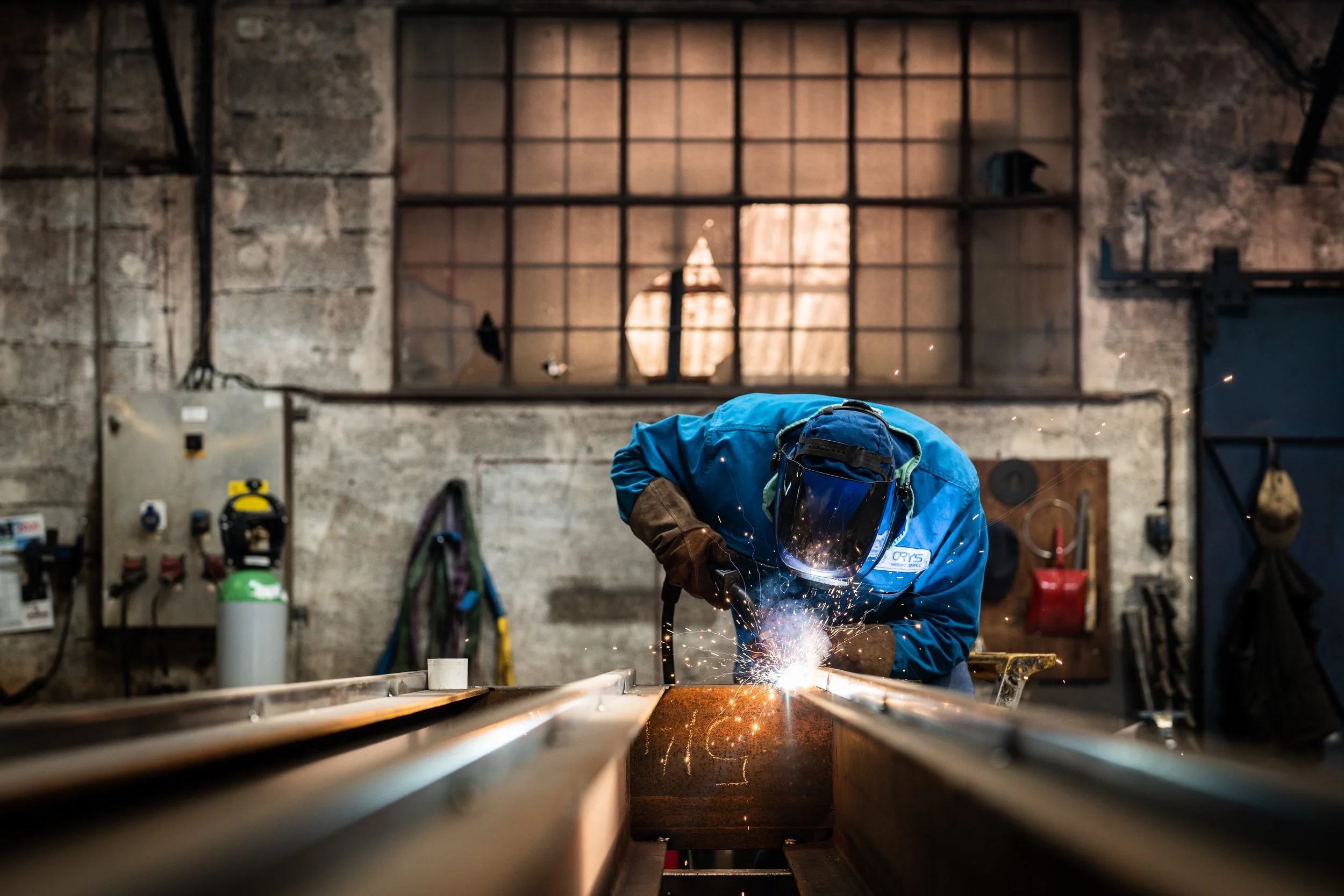 Soudeur portant un casque de protection travaillant sur une pièce métallique dans un atelier industriel.