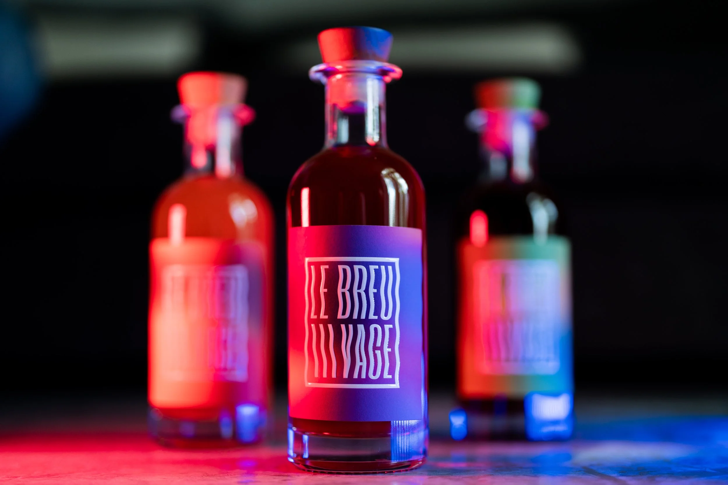 Trois fioles de liquide rouge avec une étiquette violette portant le texte « LE BREU IMAGE » sous un éclairage coloré.