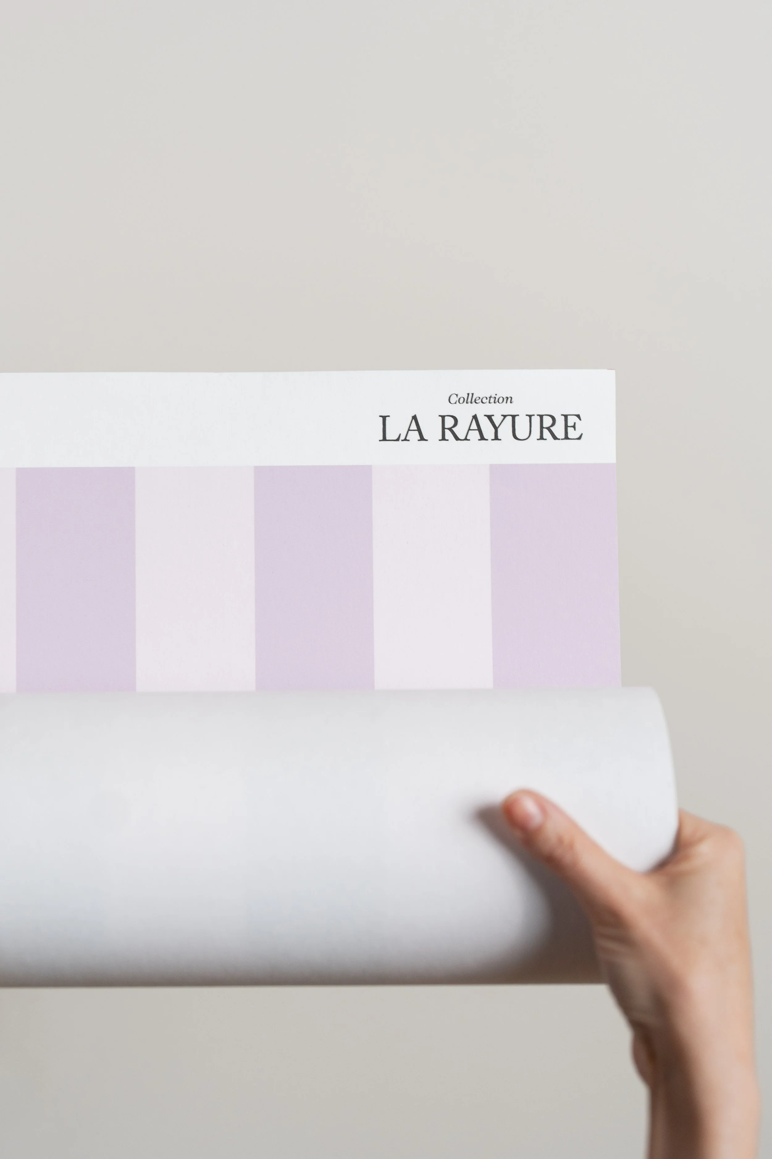 Une main tient un rouleau de papier devant une affiche avec le texte 'Collection La Rayure'.