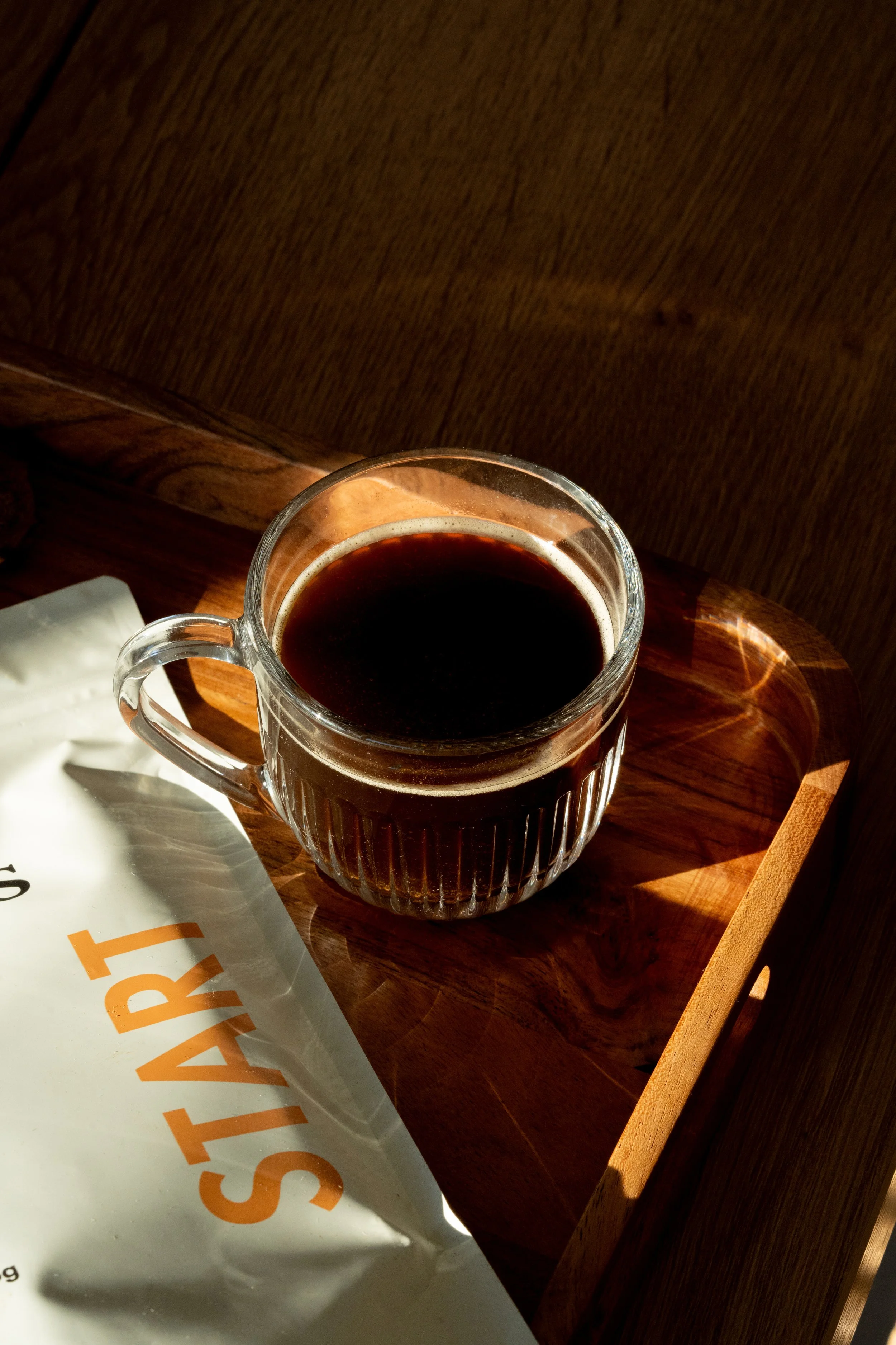Tasse en verre de café noir sur une table en bois avec un sac blanc à côté.