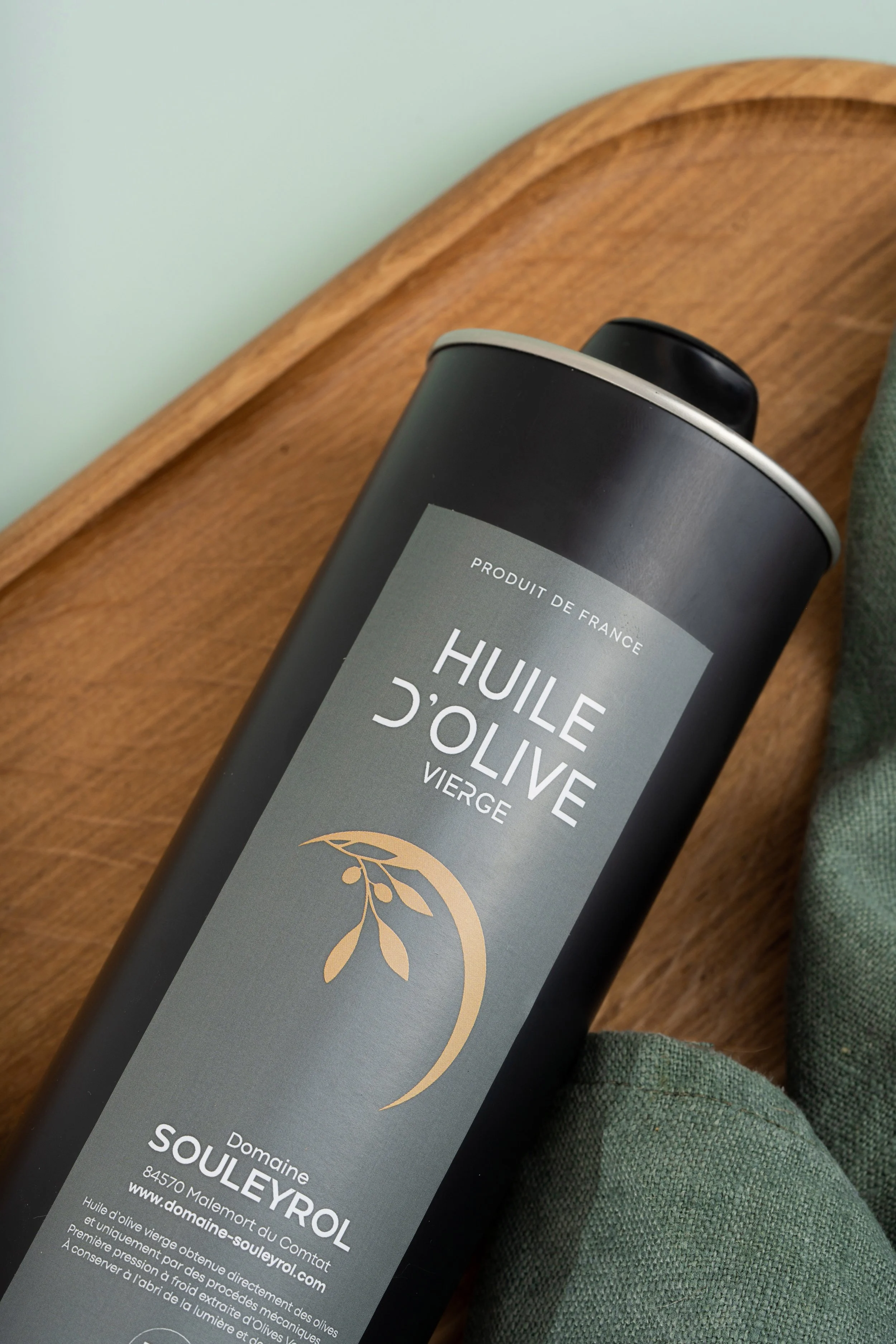 Bouteille d'huile d'olive vierge de France, de la marque Domaine Souleyrol, posée sur une table en bois avec un tissu vert à côté.