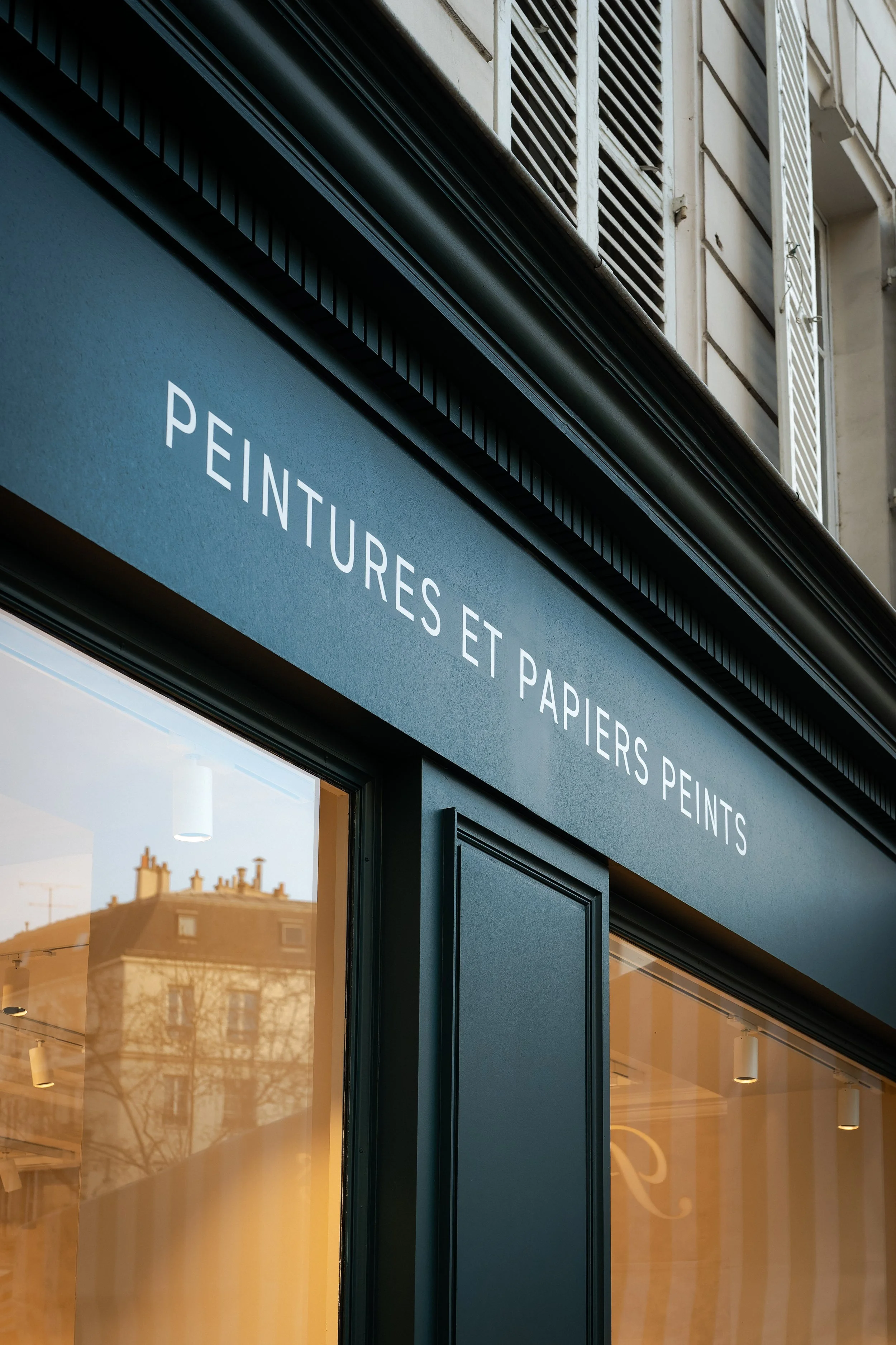 Façade d'un magasin avec une enseigne en français indiquant 'Peintures et Papiers Peints'.