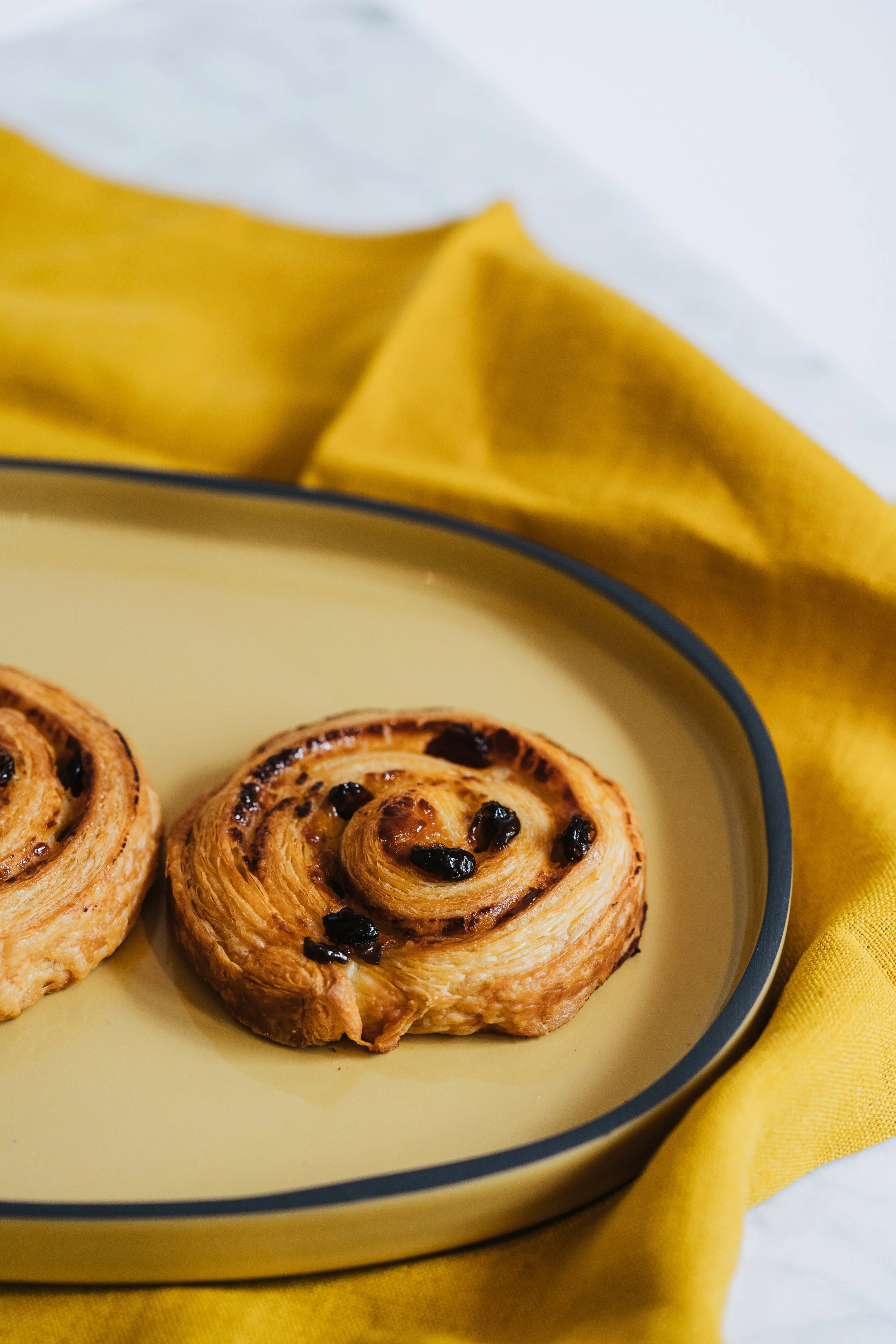 Croissants aux raisins sur une assiette jaune, avec un tissu jaune en arrière-plan.