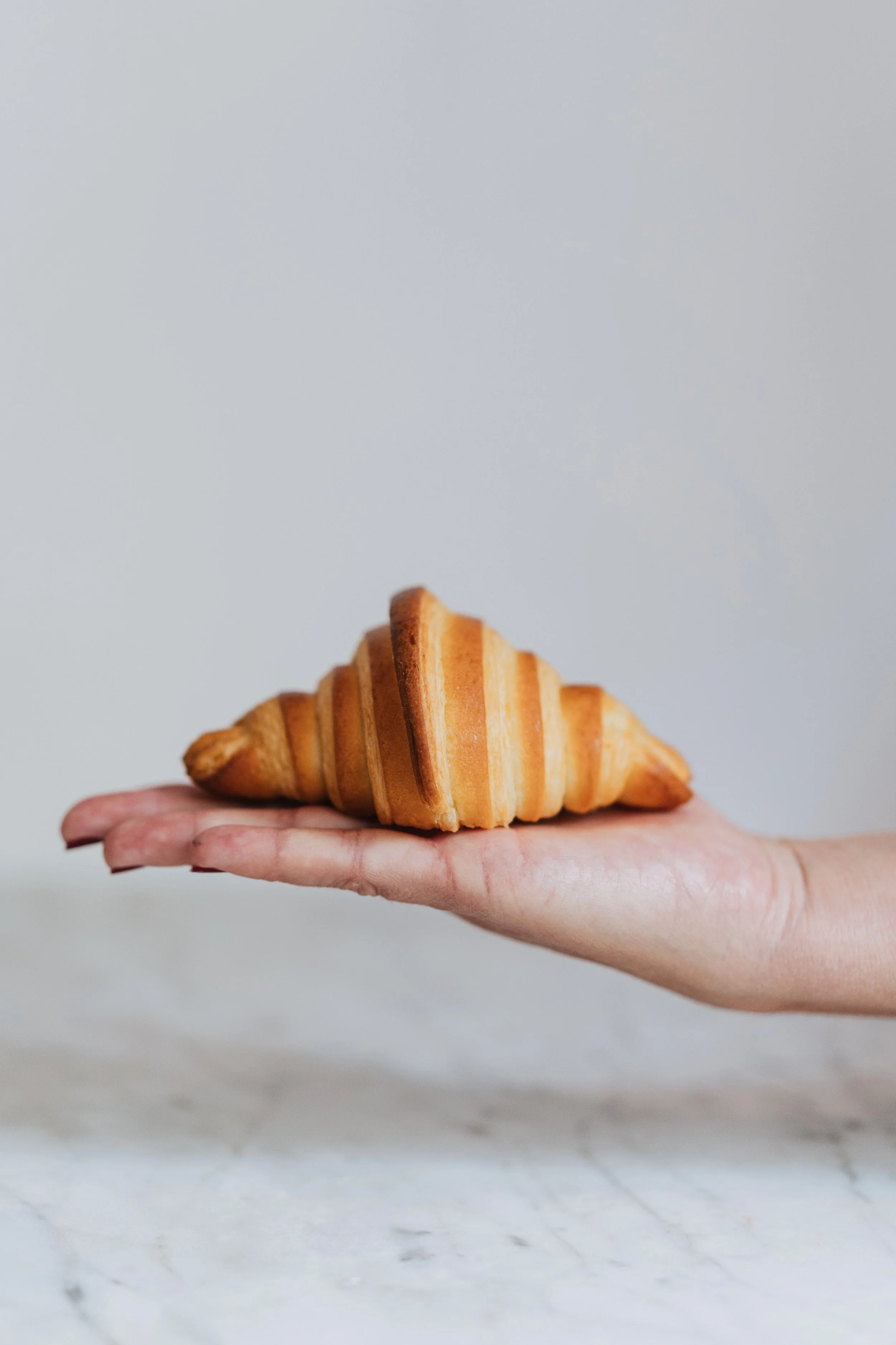 Une main tient un croissant doré sur une surface en marbre claire.
