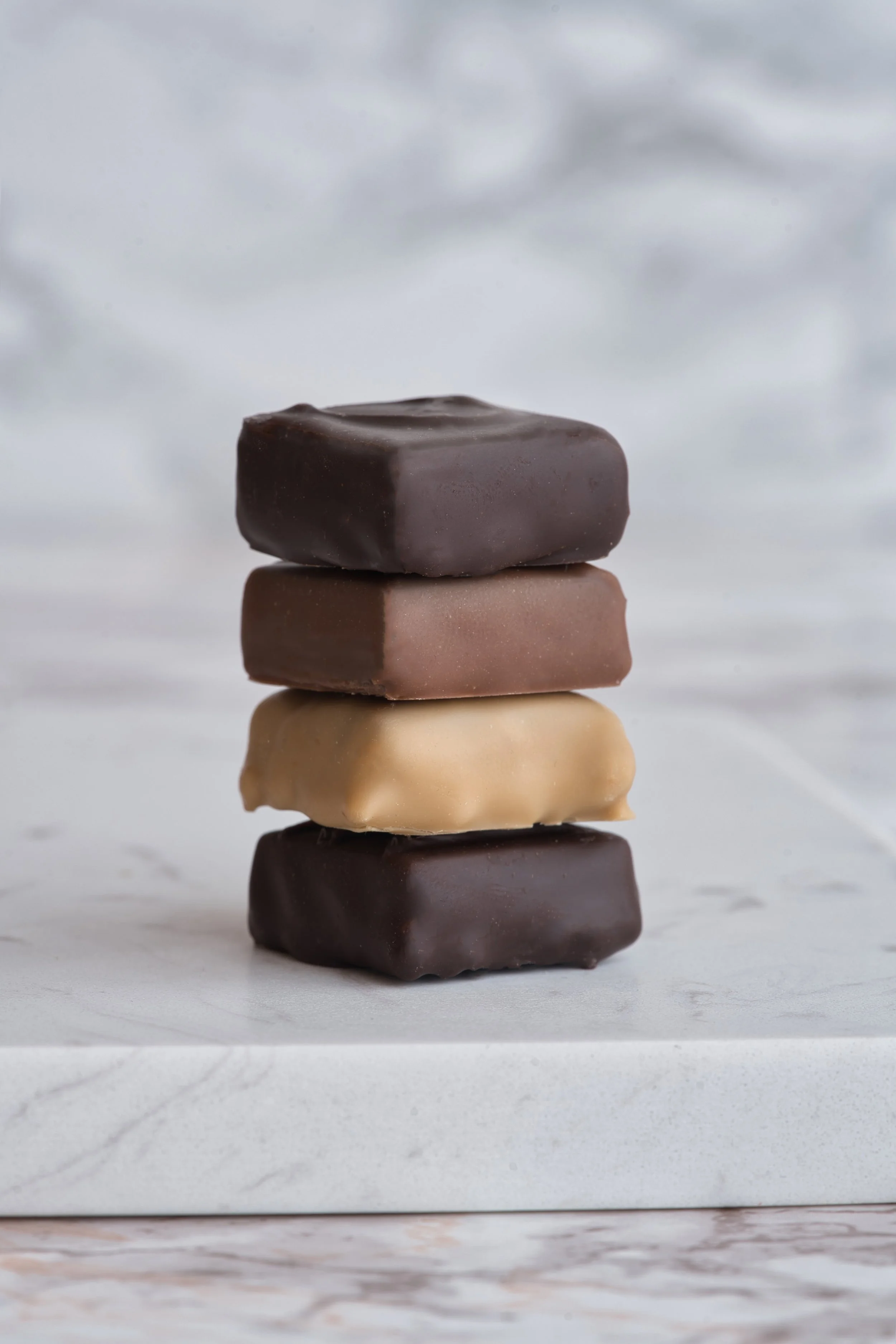 Quatre chocolats de différentes couleurs empilés sur une surface blanche