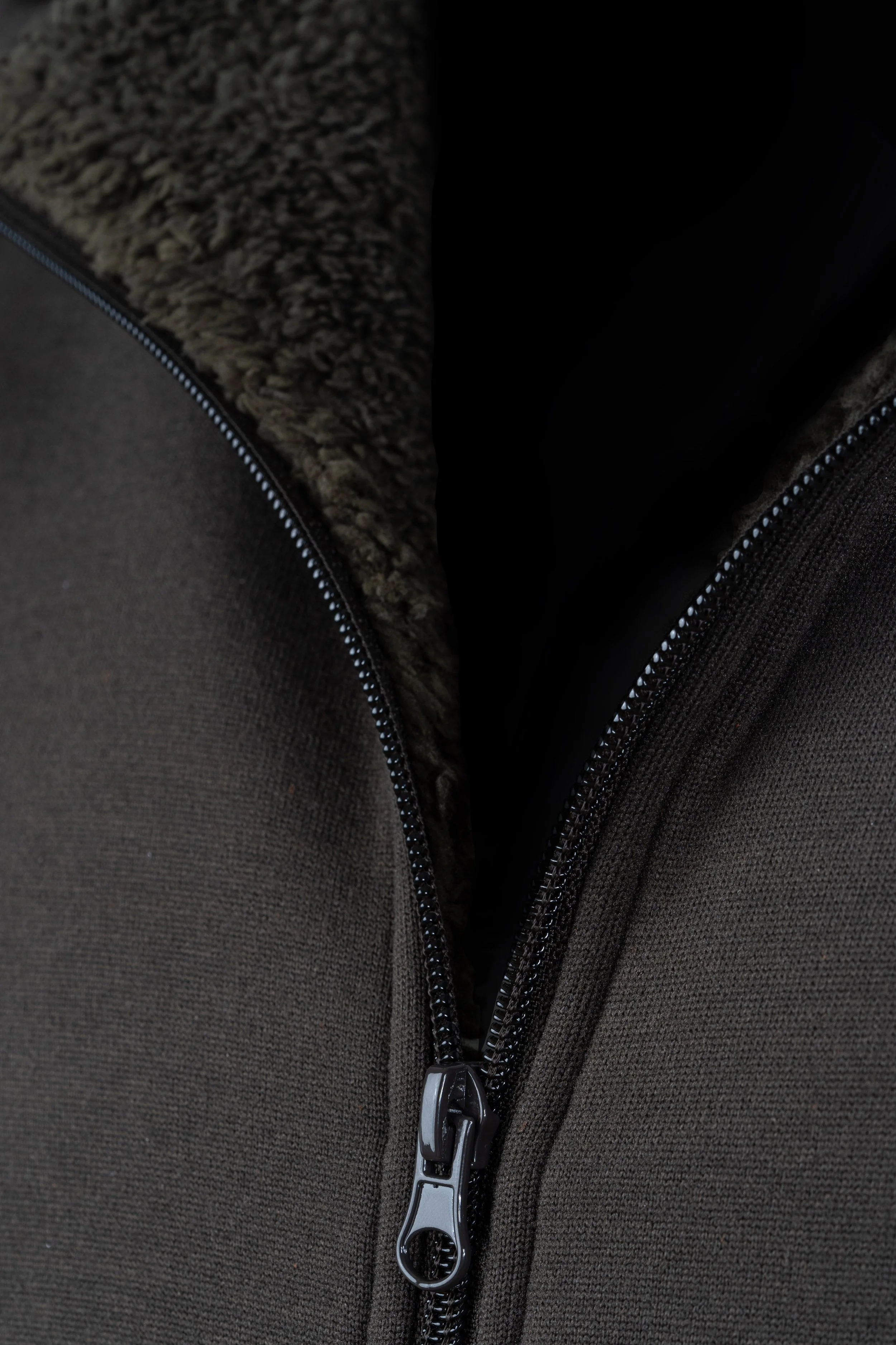 Zoom sur une fermeture éclair noire d'une veste ou d'un sac en tissu foncé avec intérieur en peluche beige.