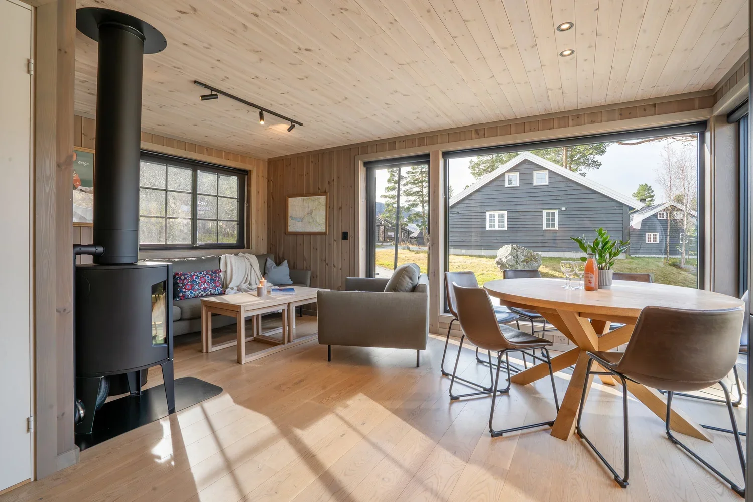 Åpen stue med store vinduer. Spisebord, sofa, sofabord og peis. Foto