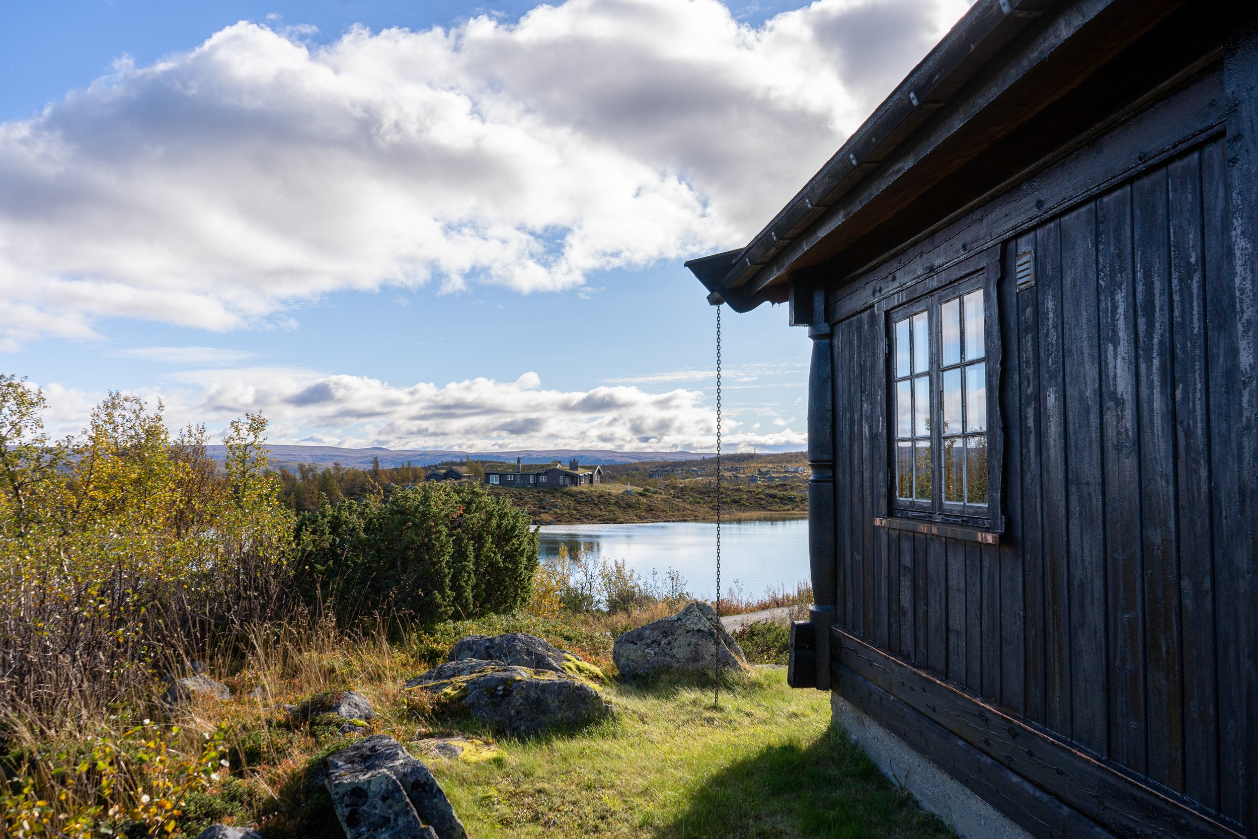 Eksteriør av hytte på fjellet, med utsikt til vann i bakgrunnen. Foto