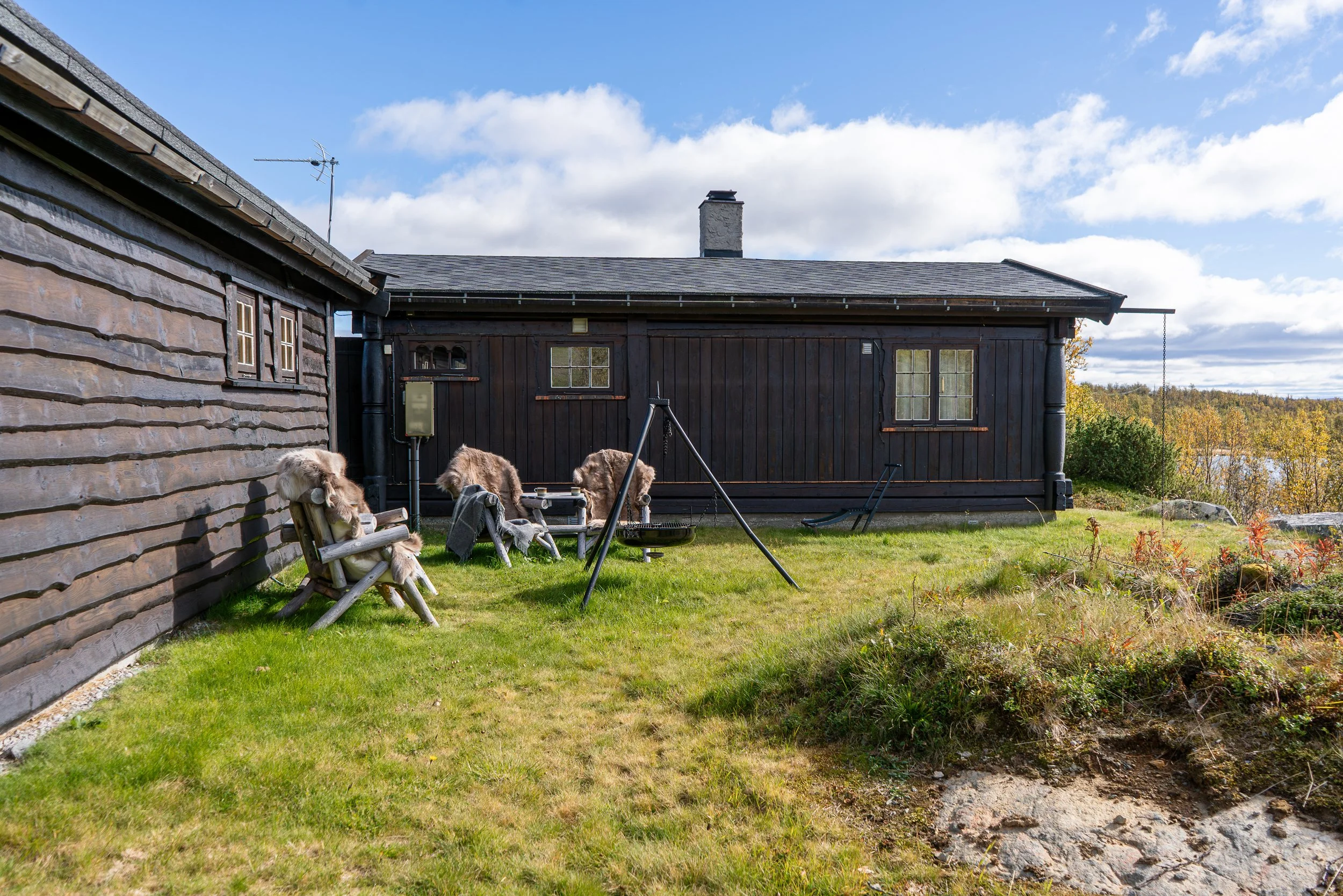 Utendørs sittegruppe med bålpanne. Hytte i bakgrunnen. Foto