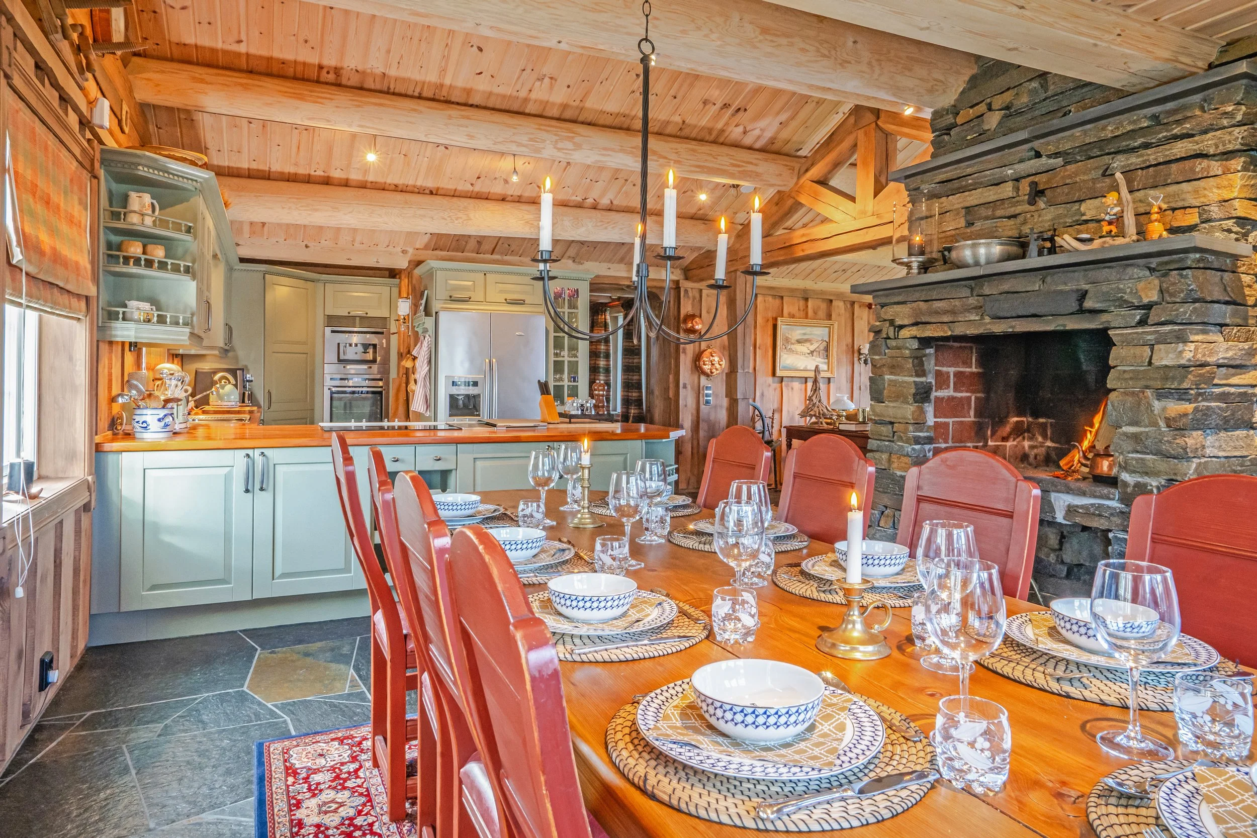 Spisestue med dekket bord. Liten peis i hjørnet, og kjøkken i bakgrunnen. Foto