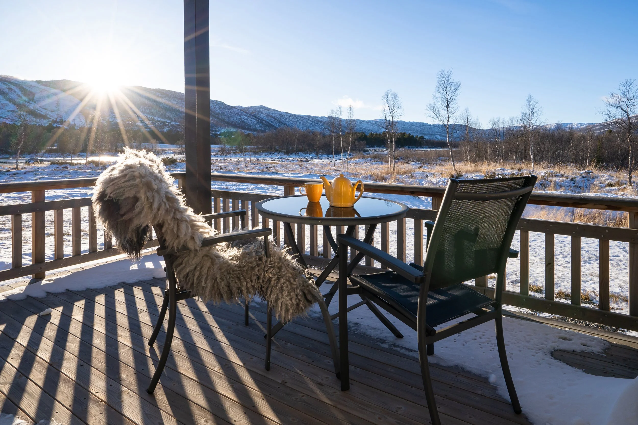 Terrasse med utemøbler. Utsikt over natur, med sol som går ned bak fjellet. Foto (Copy)