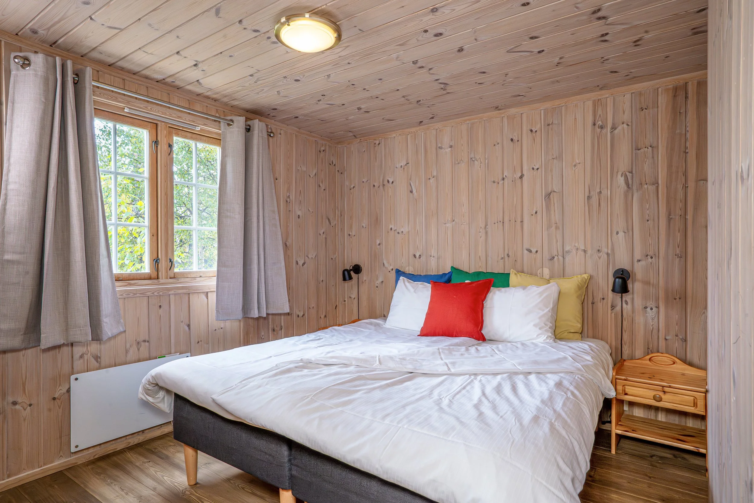 Soverom med oppredd dobbeltseng. Pynteputer i ulike farger. Foto