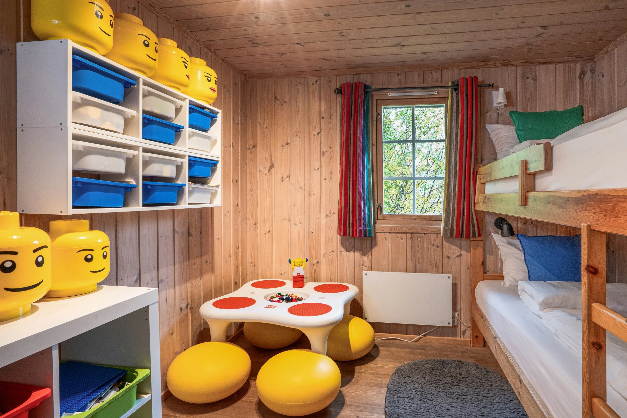 Soverom med oppredd køyeseng, LEGO-byggebord og hyller fylt med LEGO. Foto