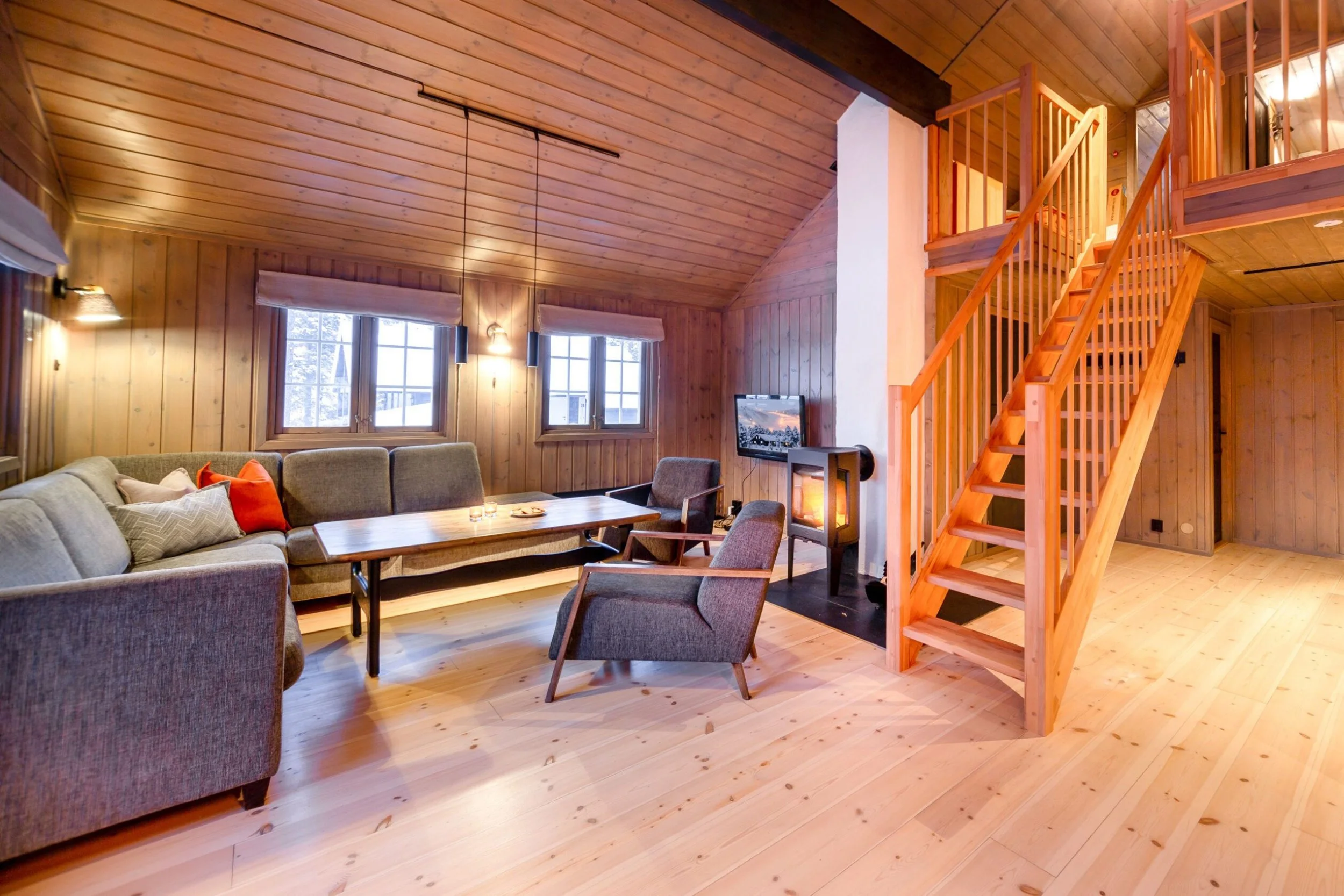 Åpen hyttestue med sofa og peis. Trapp til hems på siden. Foto